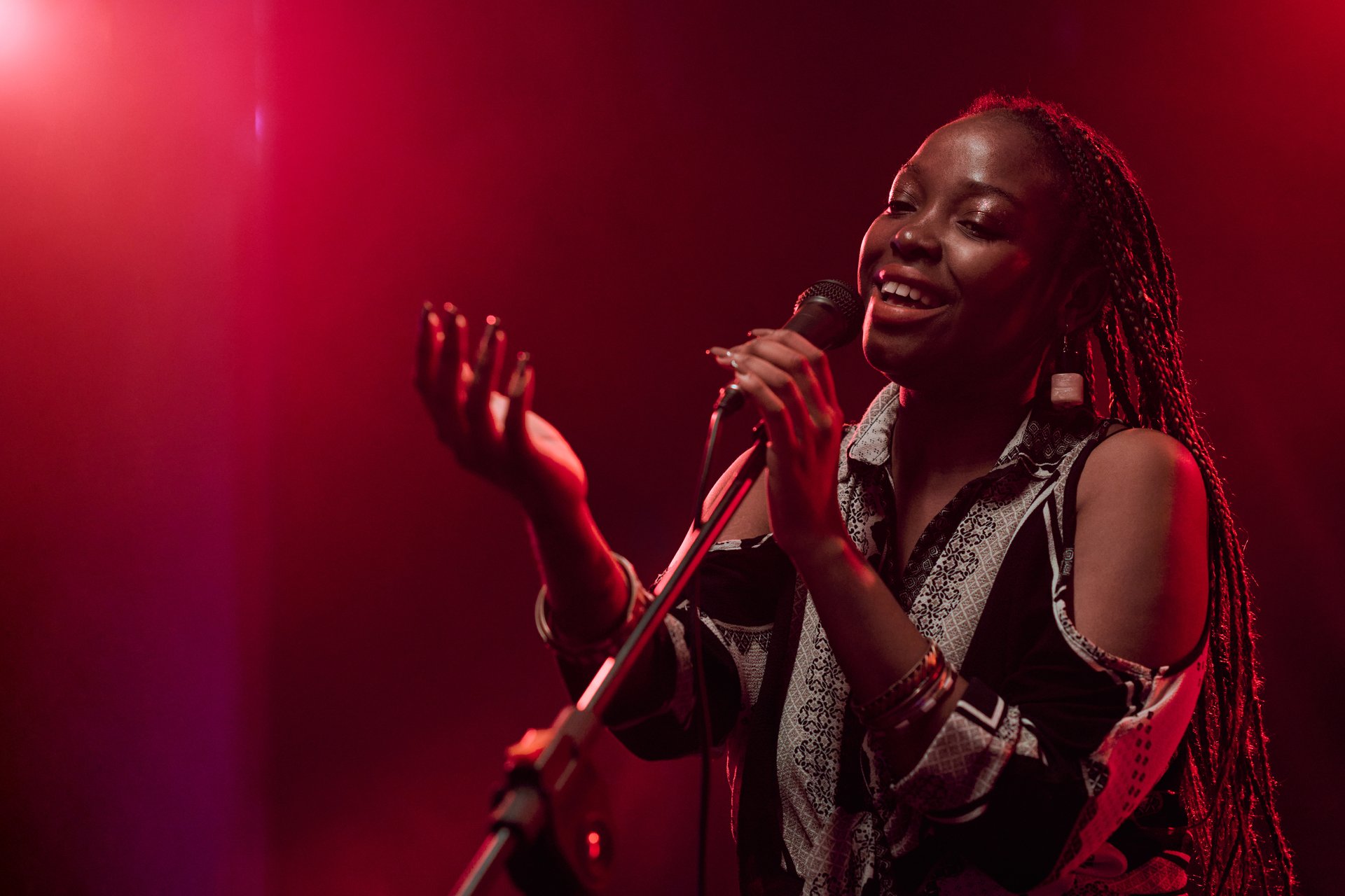 Waist up portrait of talented Black woman singing into microphone performing on stage in dim red lights copy space