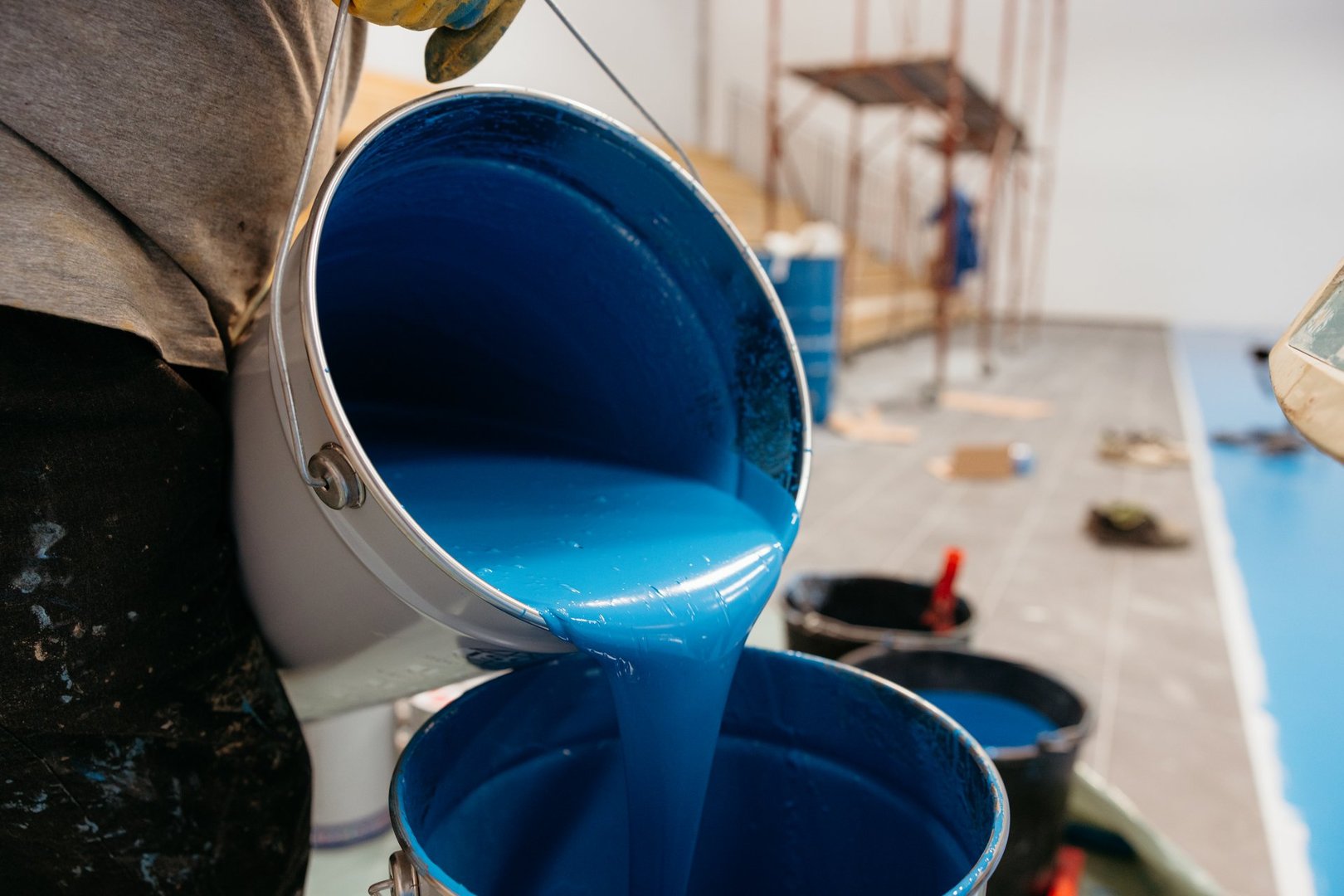 Construction worker pouring blue epoxy resin from a bucket into another bucket on a construction site