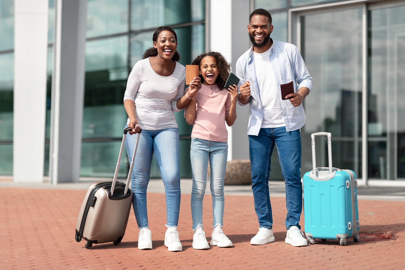 Finally Vacation. Cheerful positive black family of three people holding passports with tickets and shaking clenched fists, making winner gesture, travelling together standing near airport terminal