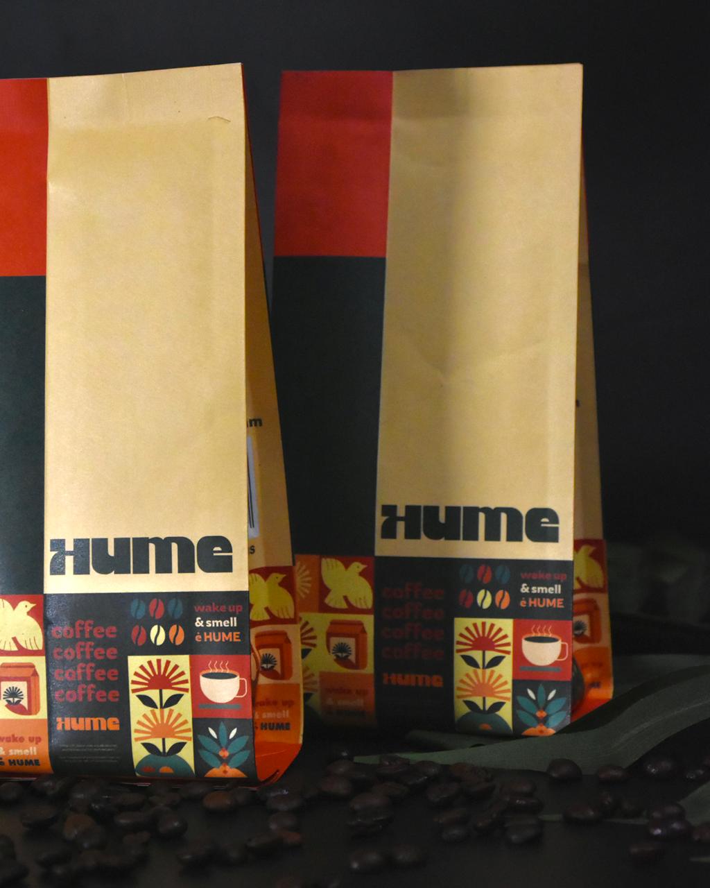 Two Hume coffee bags with colorful designs on a dark background, surrounded by scattered coffee beans.