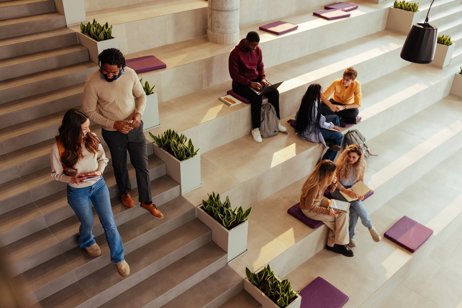 Diverse university students are walking and studying in a modern open space with bleachers, plants and natural light