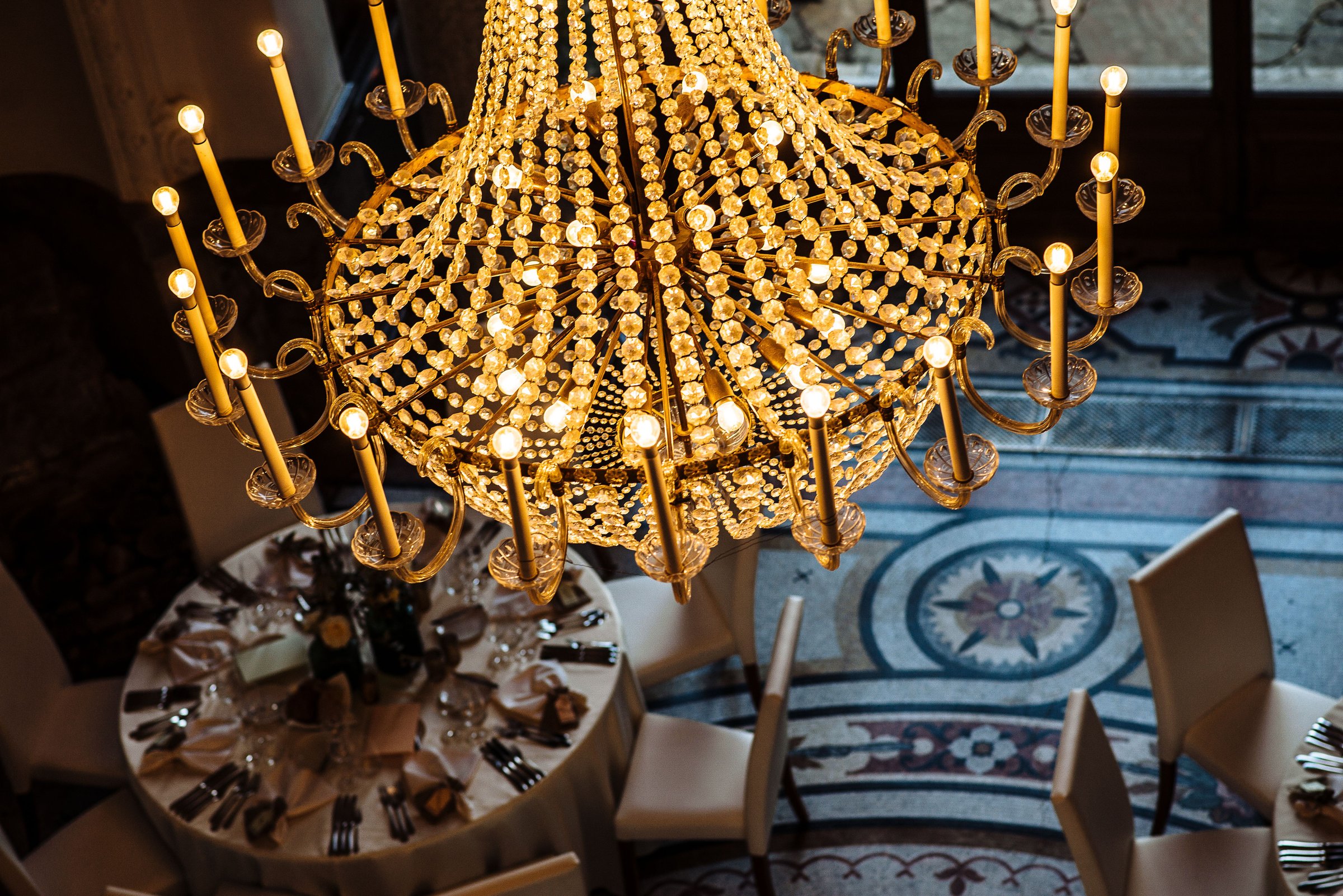 Elegant chandelier above a decorated dining table in a luxurious setting, showcasing intricate design and opulence.