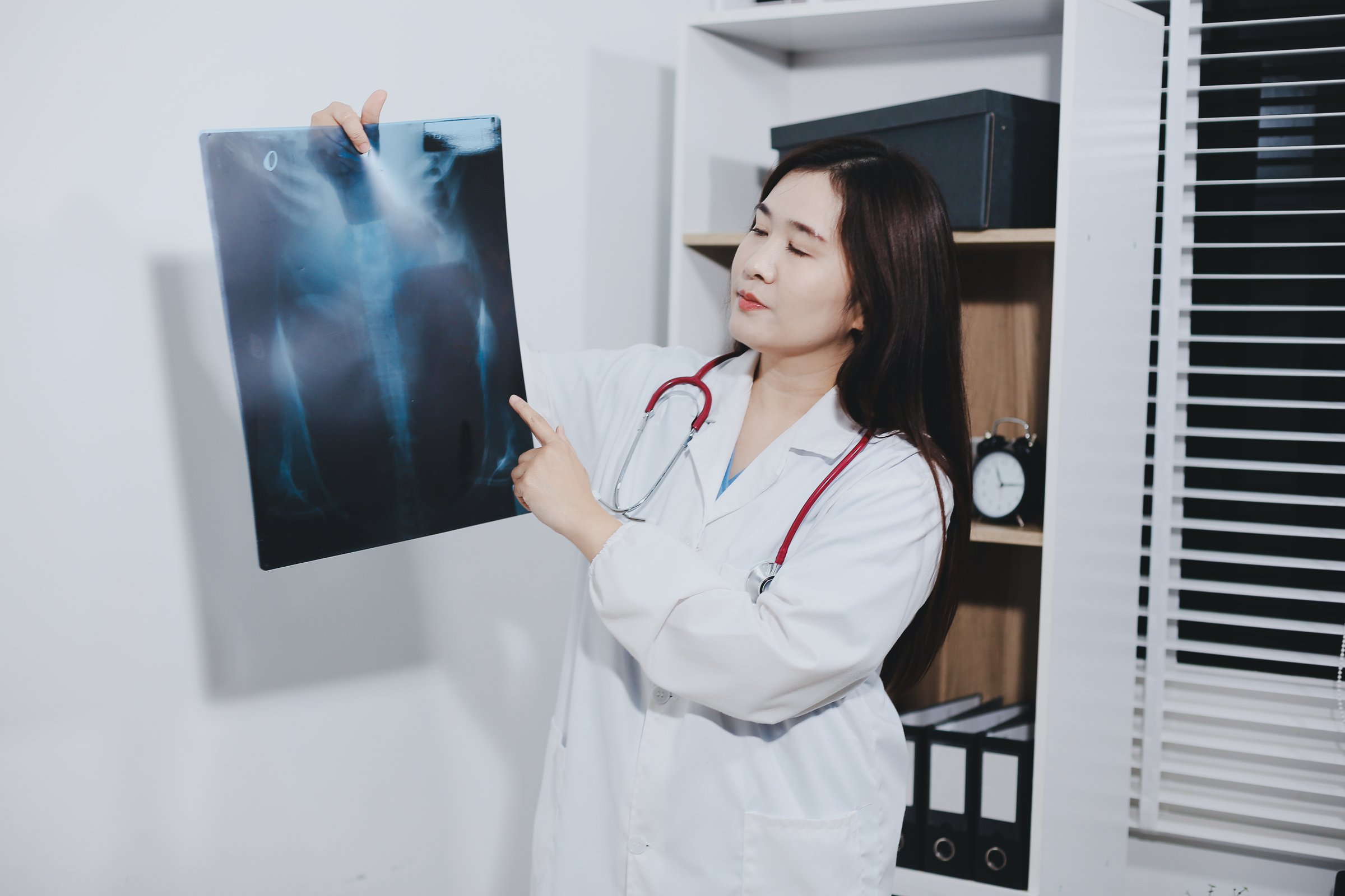 Asian Muslim doctor in hijab and scrubs headphones around her neck Stand confidently in the medical office, isolated on white background, holding x-ray film.
