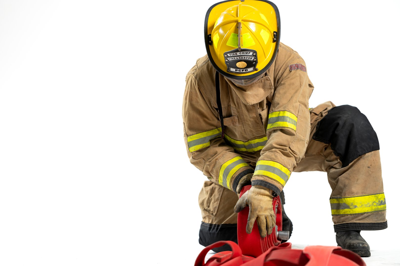 Full-body studio portrait of a firefighter in protective uniform holding a firefighting and fire hose nozzle. The individual stands confidently against a white background