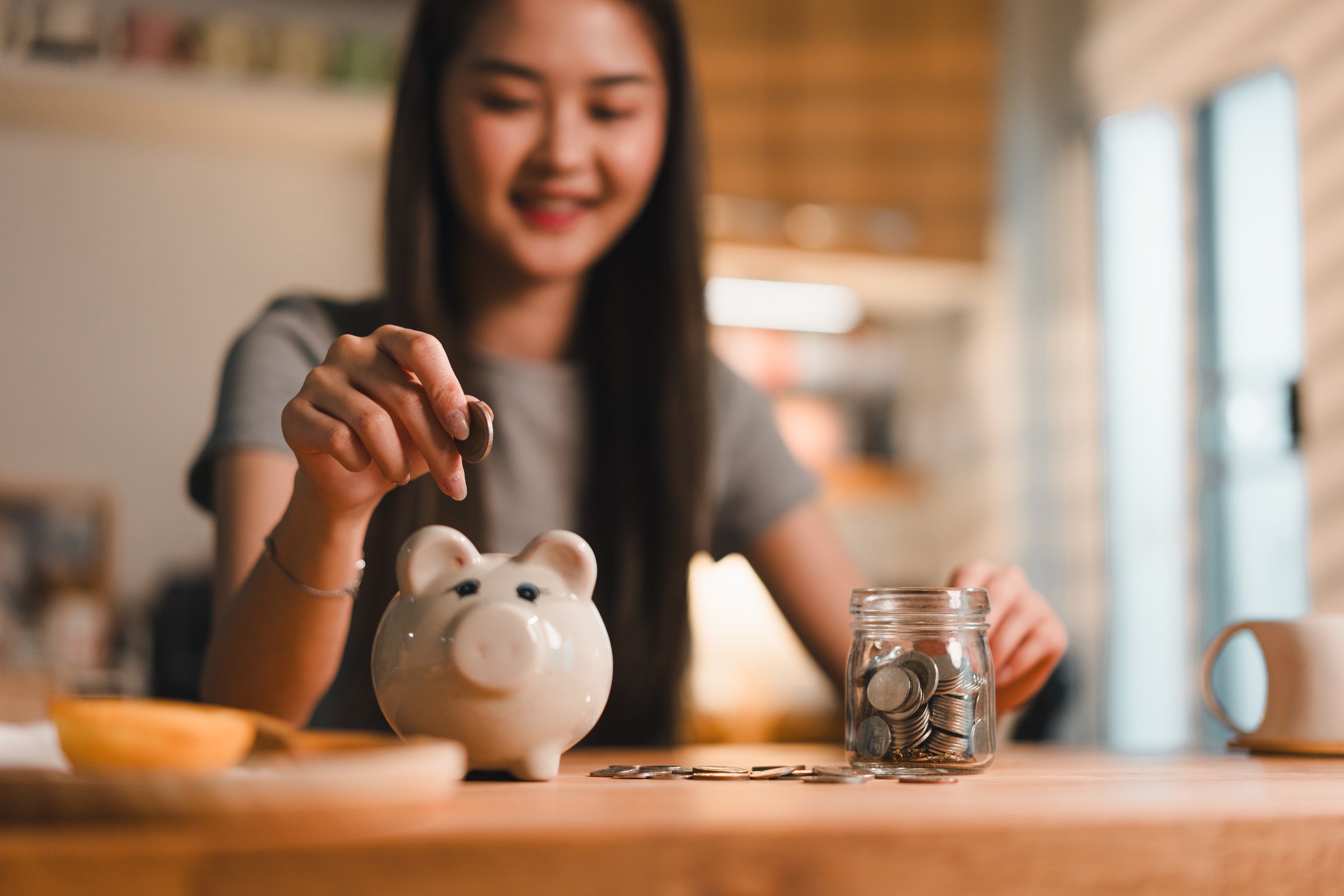 Saving money is important habit, as shown by young woman joyfully depositing coins into piggy bank while surrounded by jar of coins. This scene captures essence of financial responsibility and.