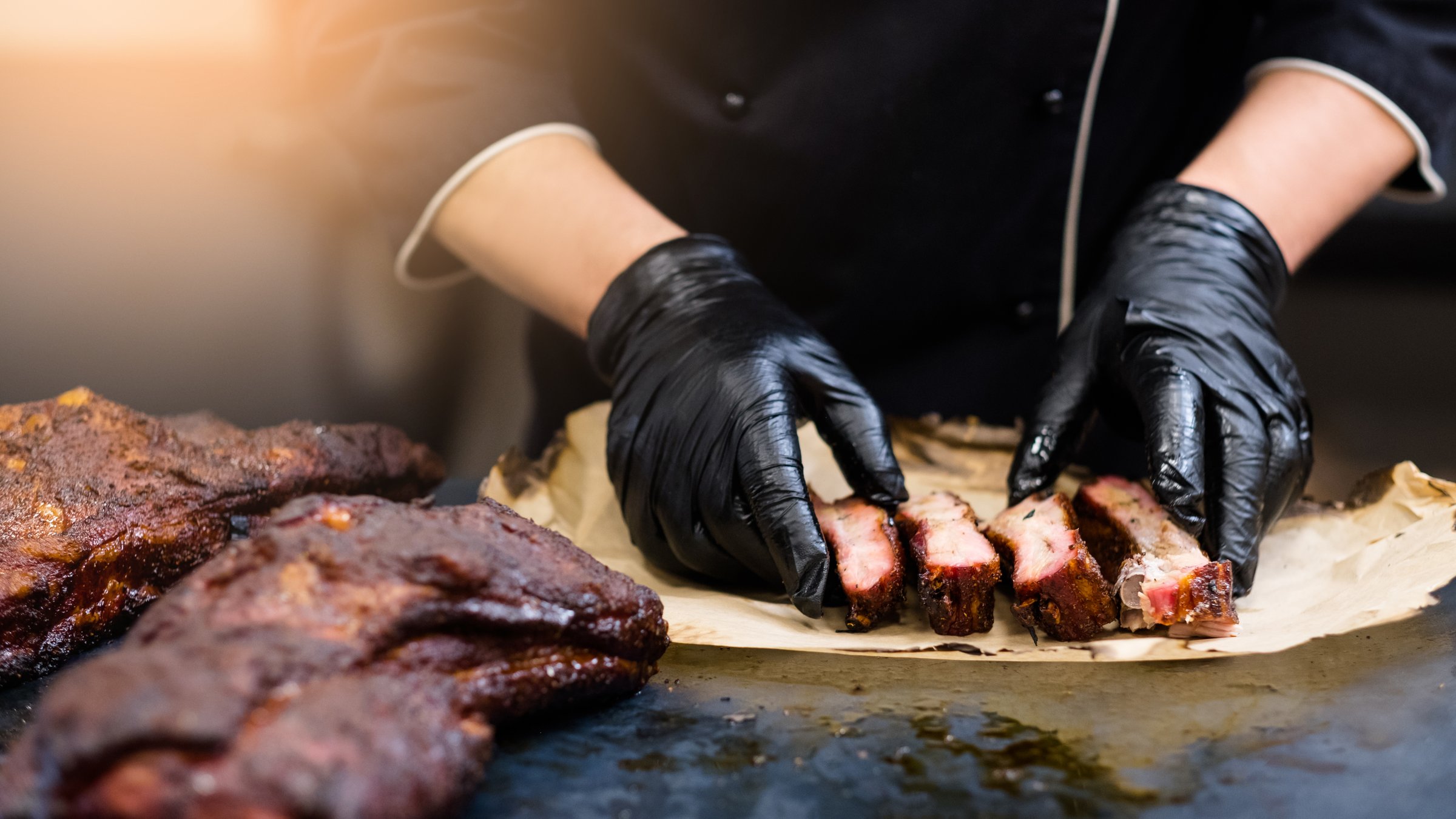 Chef profesional usando guantes de nitrilo negros en cocina de restaurante grill preparando costillas ahumadas en México