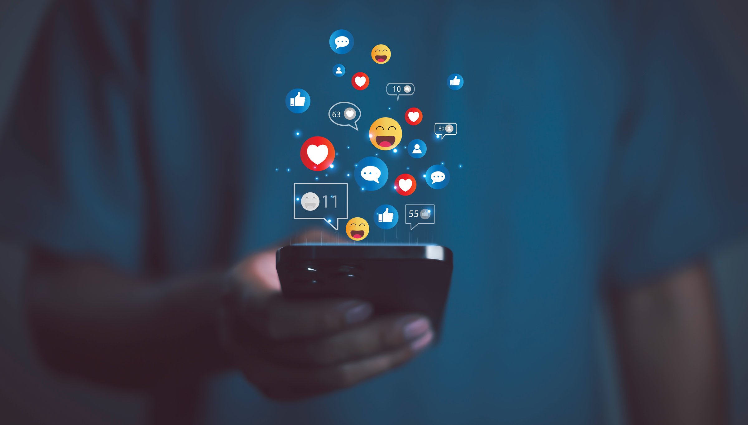 Person using smartphone with social media icons, likes, hearts, and emojis floating, symbolizing online communication, digital marketing, social network engagement, and modern lifestyle.