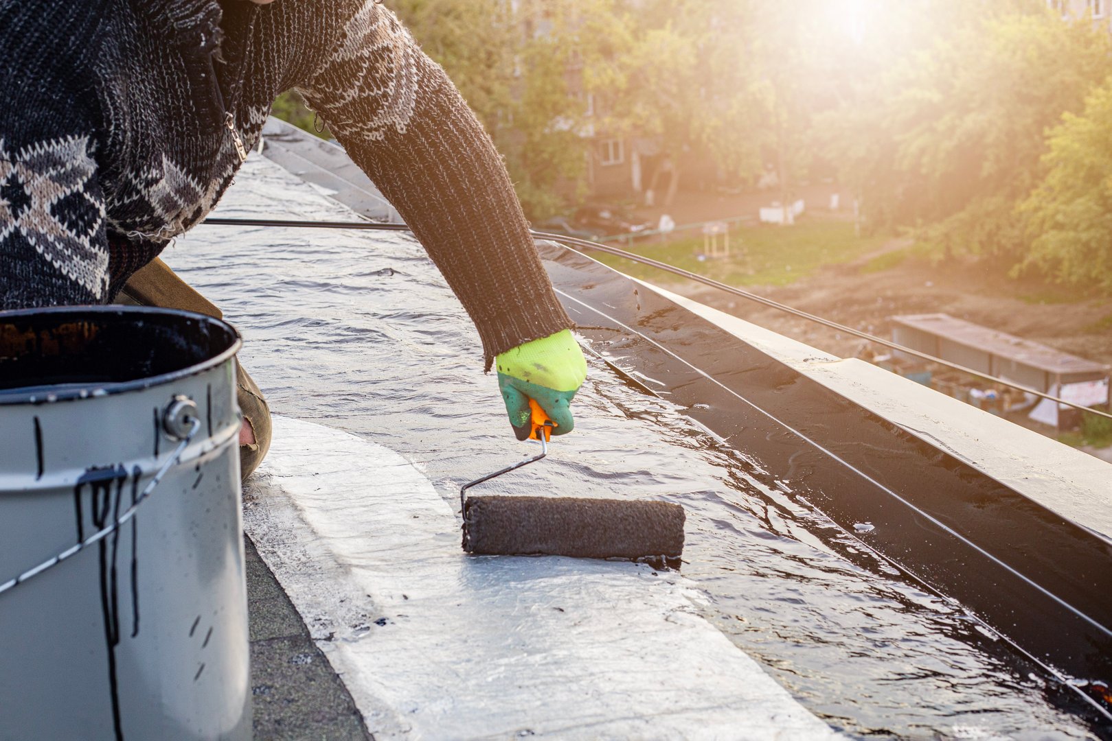 a young worker treats a roof with bitumen primer before applying rolled asphalt roofing using a torch