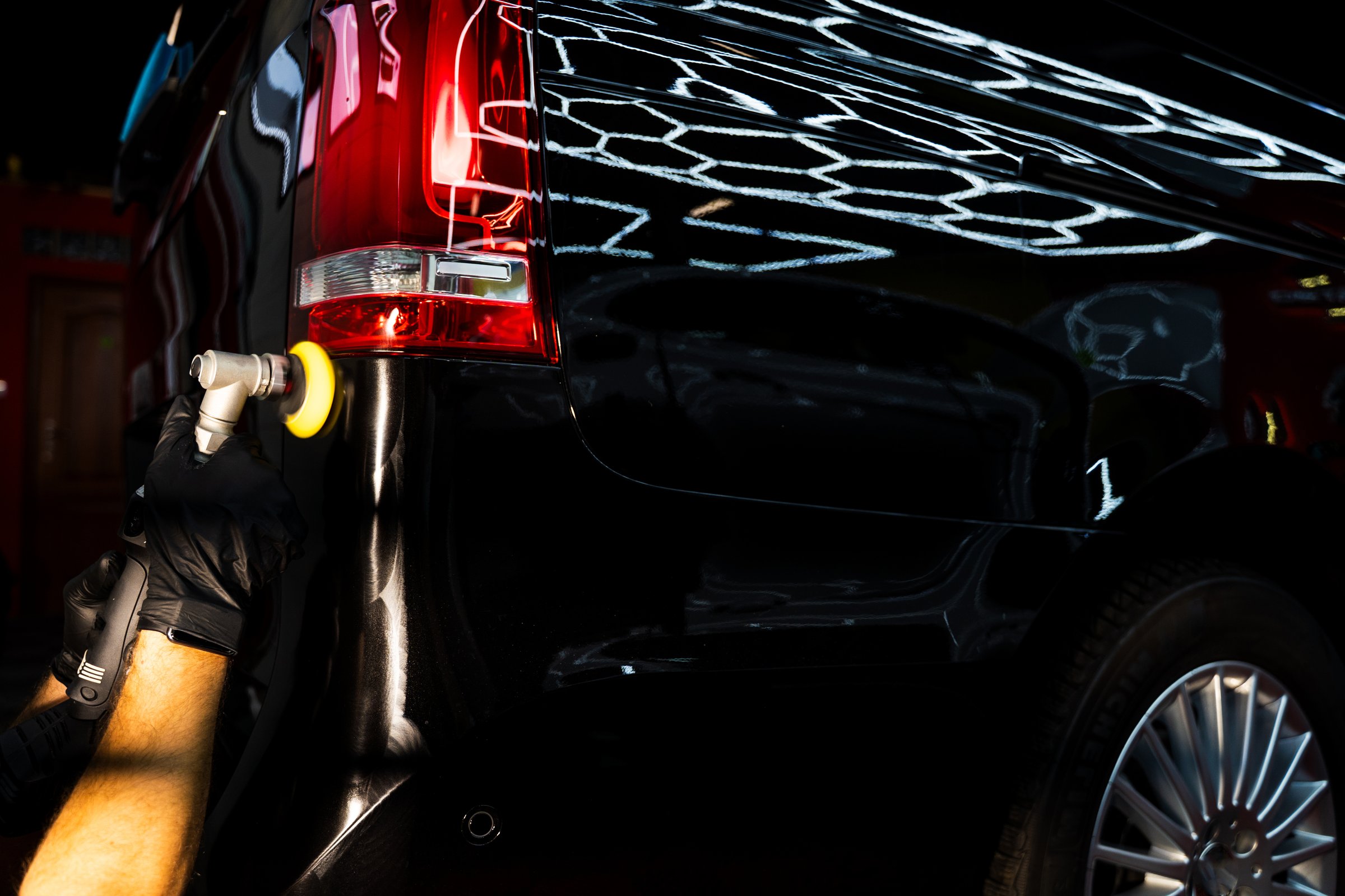 Detailer performs cutting-stage polishing with rotary machine. Aggressive paint correction using rotary polisher and hard foam pad removes deep swirls and oxidation on black paint