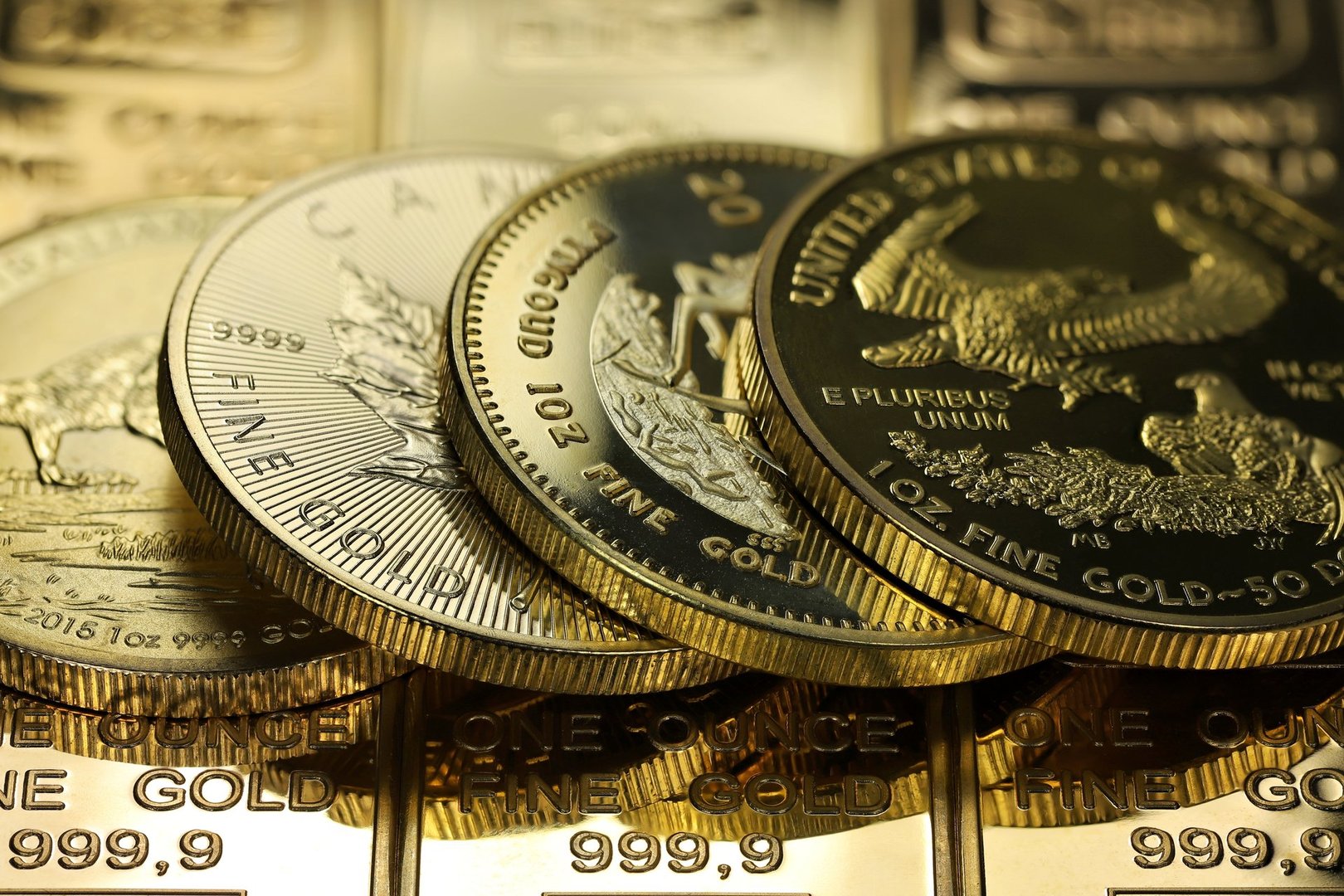 4 different 1 ounce gold bullion coins on a layer of gold ingots