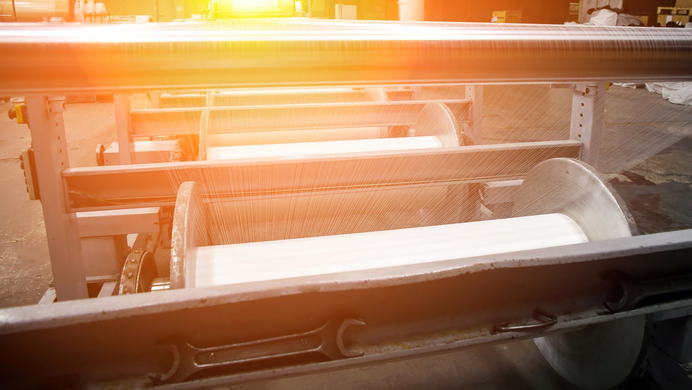 An industrial knitting machine in a textile factory with spools of white thread on a production line. Weaving fabric from yarn in a clean, well-lit manufacturing environment.
