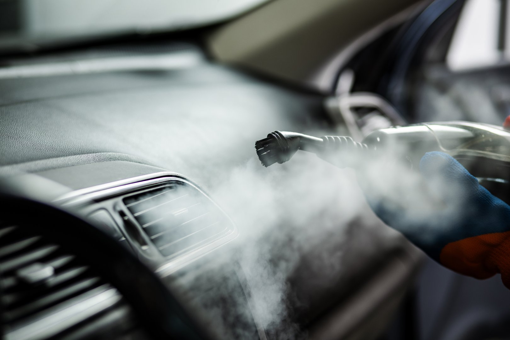 A worker utilizes a steam cleaner to deep clean the dashboard and air vents of a car, enhancing its cleanliness and freshness for the customer.