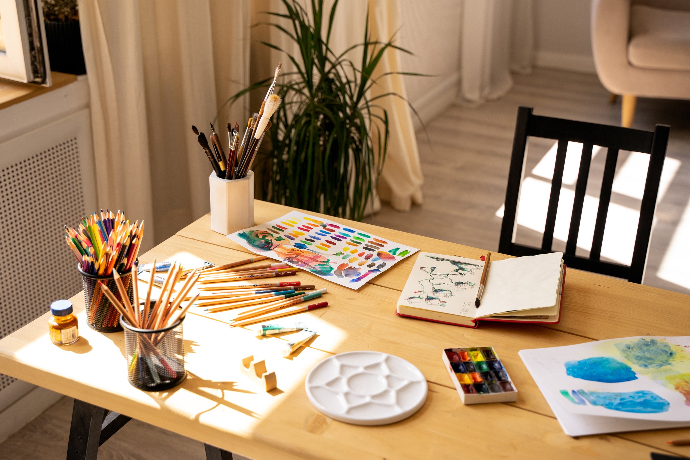 The artist's workplace with watercolor paints, gouache, brushes and sheets of paper on a wooden background.