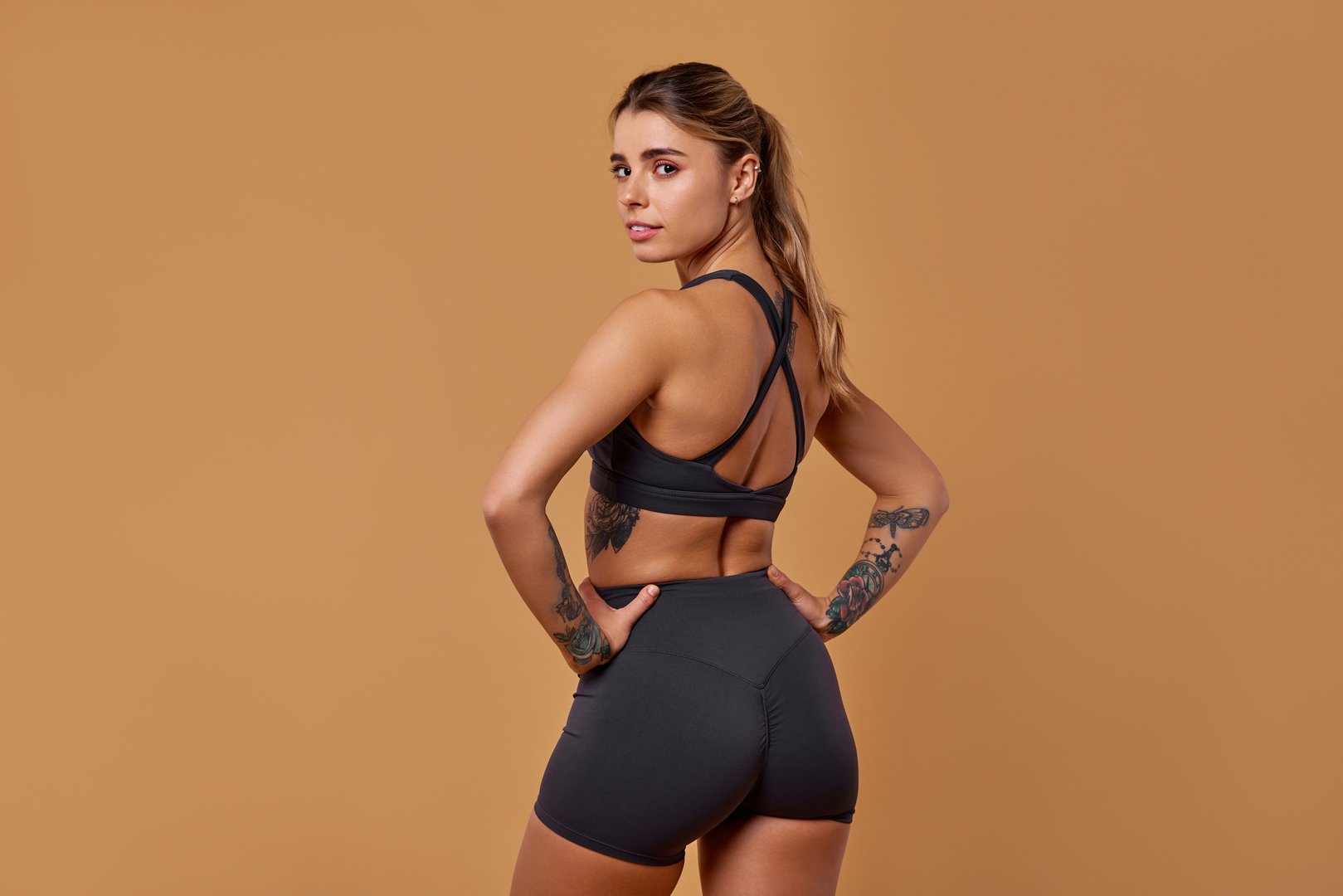 A fit and healthy woman showcases her trendy, stylish athletic wear while posing with confidence and grace against a warm, minimalist backdrop that enhances her vibrant presence and attitude