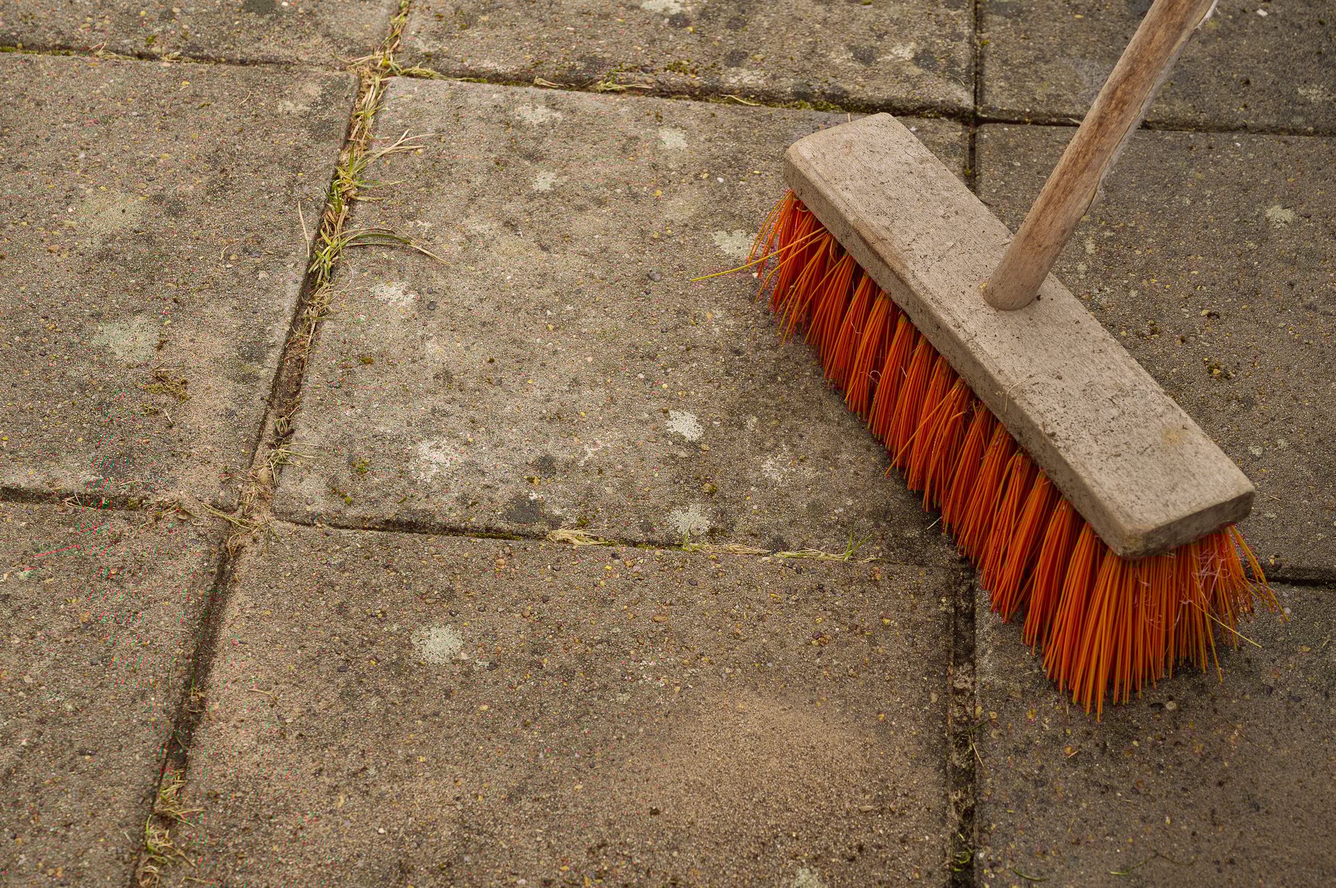 Terrassenreinigung Ergebnis - roter Besen steht auf frisch gereinigten Gartenplatten