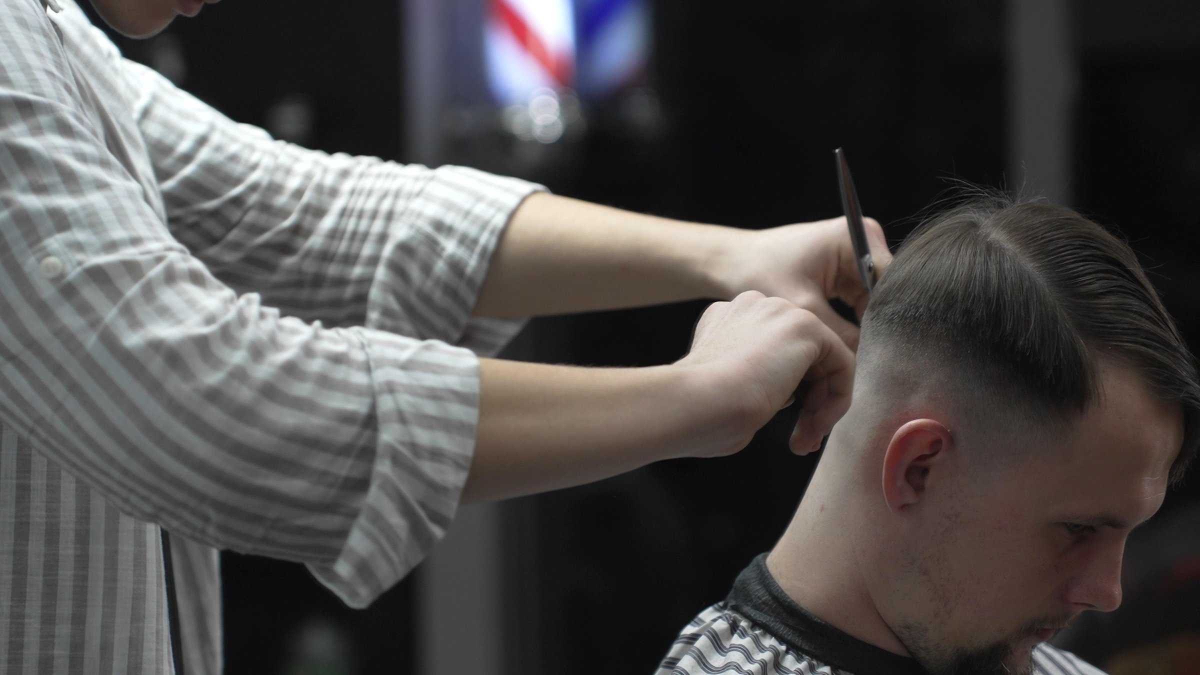 Professional barber combing client hair before haircut, preparing for styling in barbershop, creating modern hairstyle for men, beauty salon service