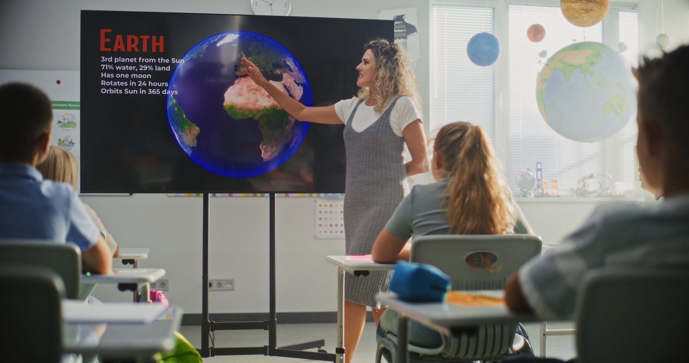 Elementary School Students Studying Basic Information About Solar System and Planets in Modern Classroom. Female Teacher Educating Smart Diverse Kids During Astronomy Lesson Using Digital Screen.