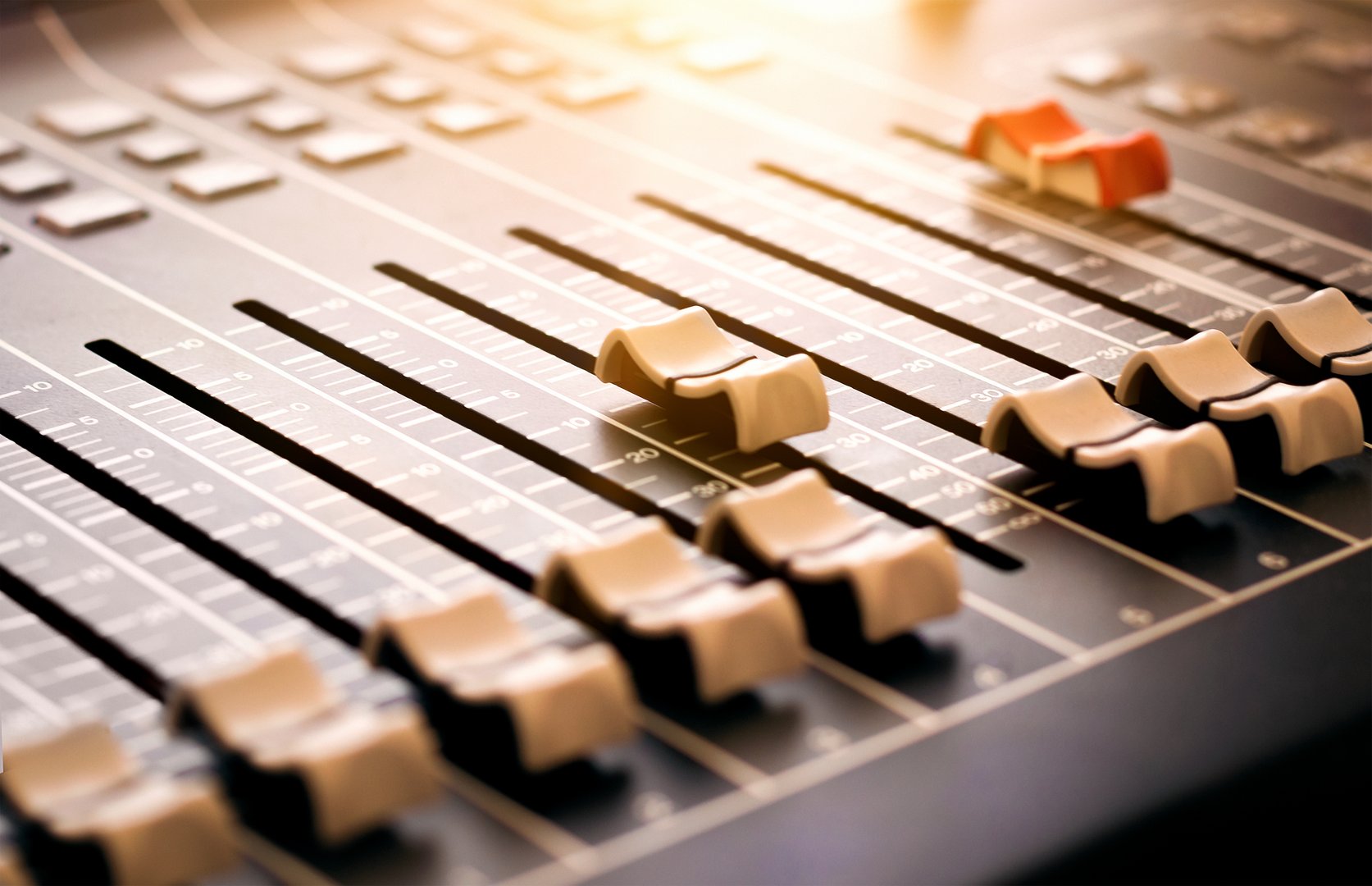 Music Mixer Desk – abstract of professional audio recording mixing board. A row of console faders controls to adjust level of multiple sound input sources and combine signals. Focus on studio slider.