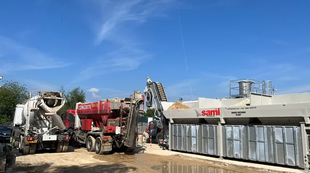 Parked cement trucks and crane with concrete discharge hose on provincial street, supply cement to construction site in background on a sunny day in Gulpen, South Limburg, the Netherlands
