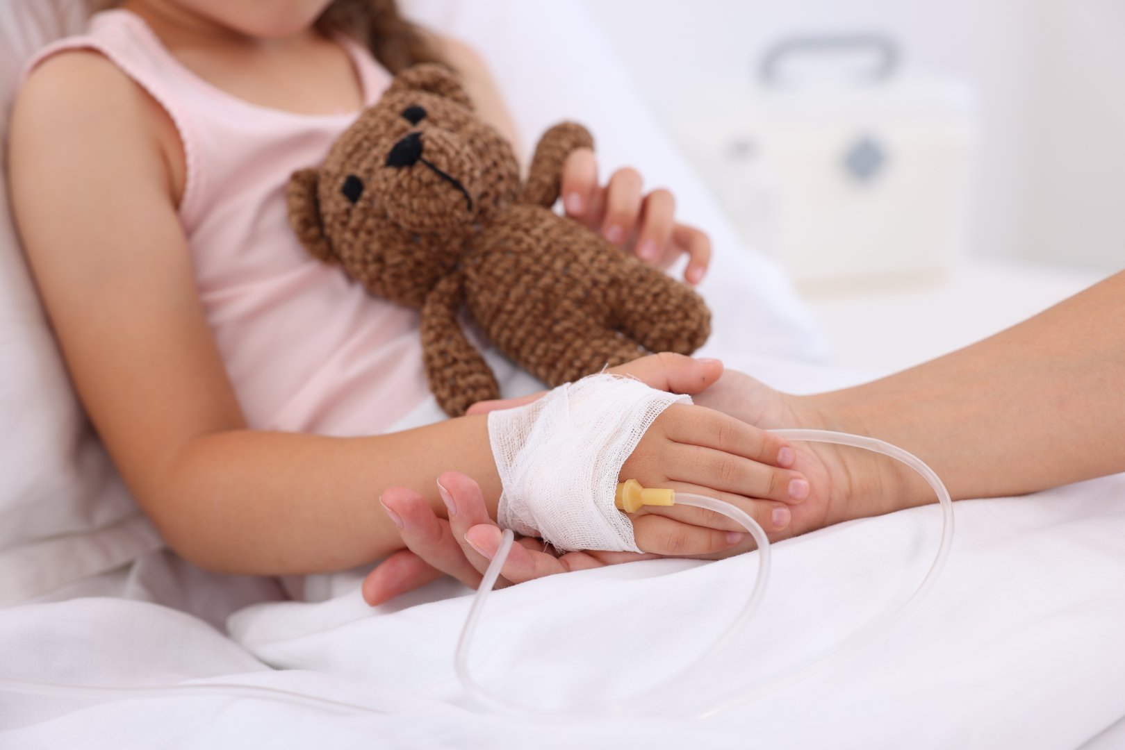 Mother and her little daughter with IV drip on bed in hospital, closeup