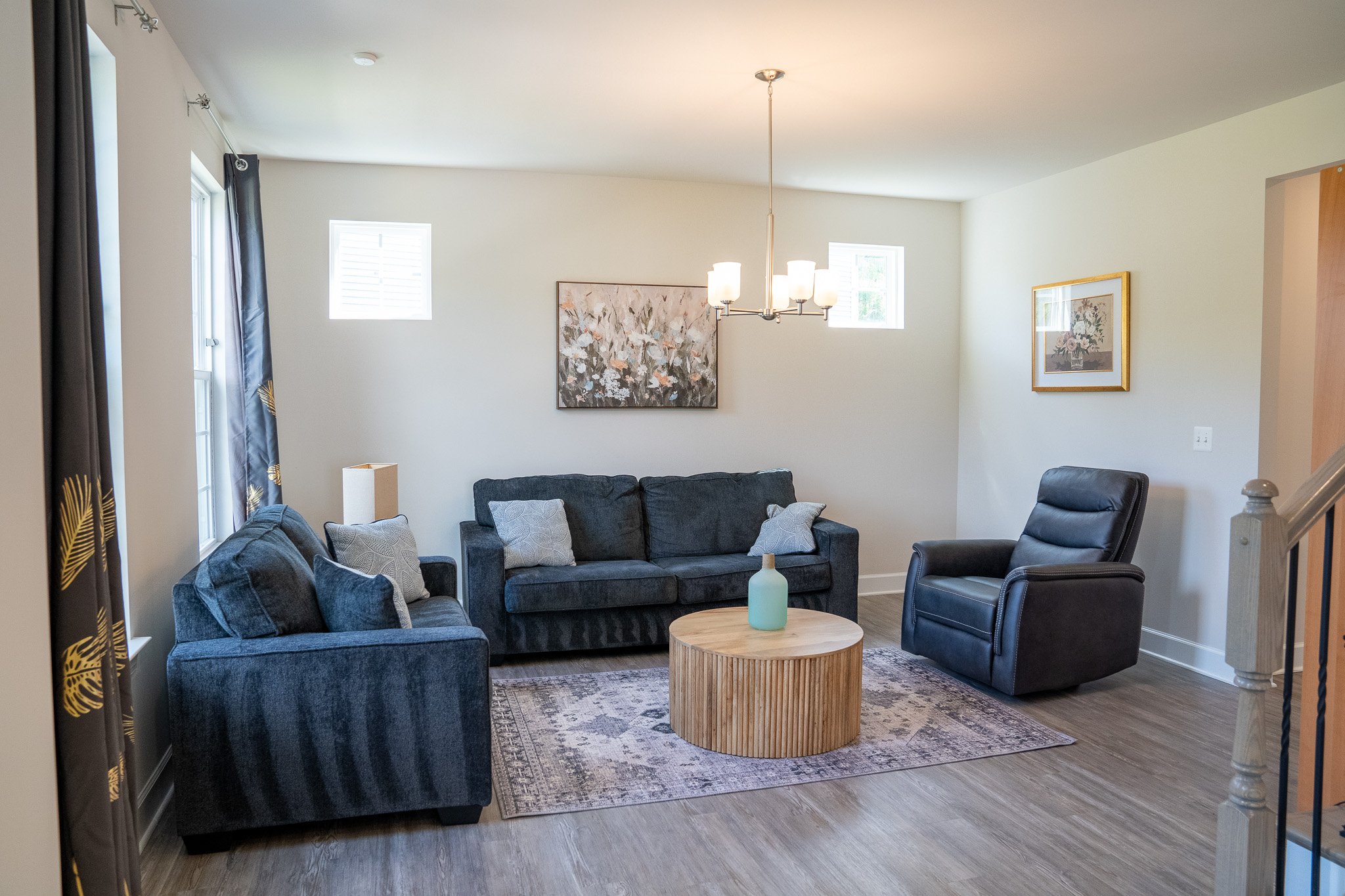 Modern living room with blue sofas, a round wooden coffee table, a chandelier, and wall art.