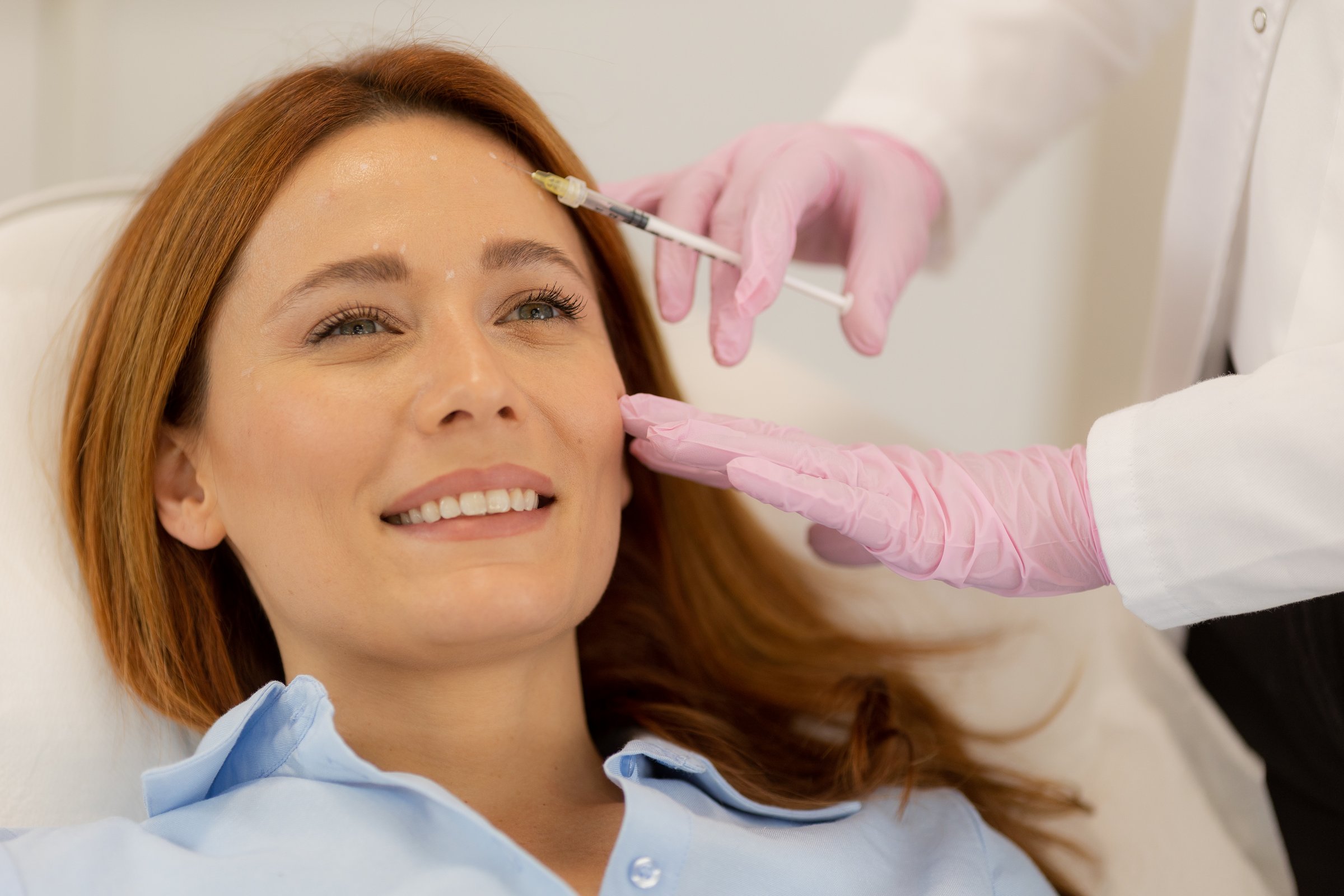 Client sits comfortably in a bright clinic, smiling as a professional applies dermal filler treatment. The serene atmosphere supports relaxation and rejuvenation.