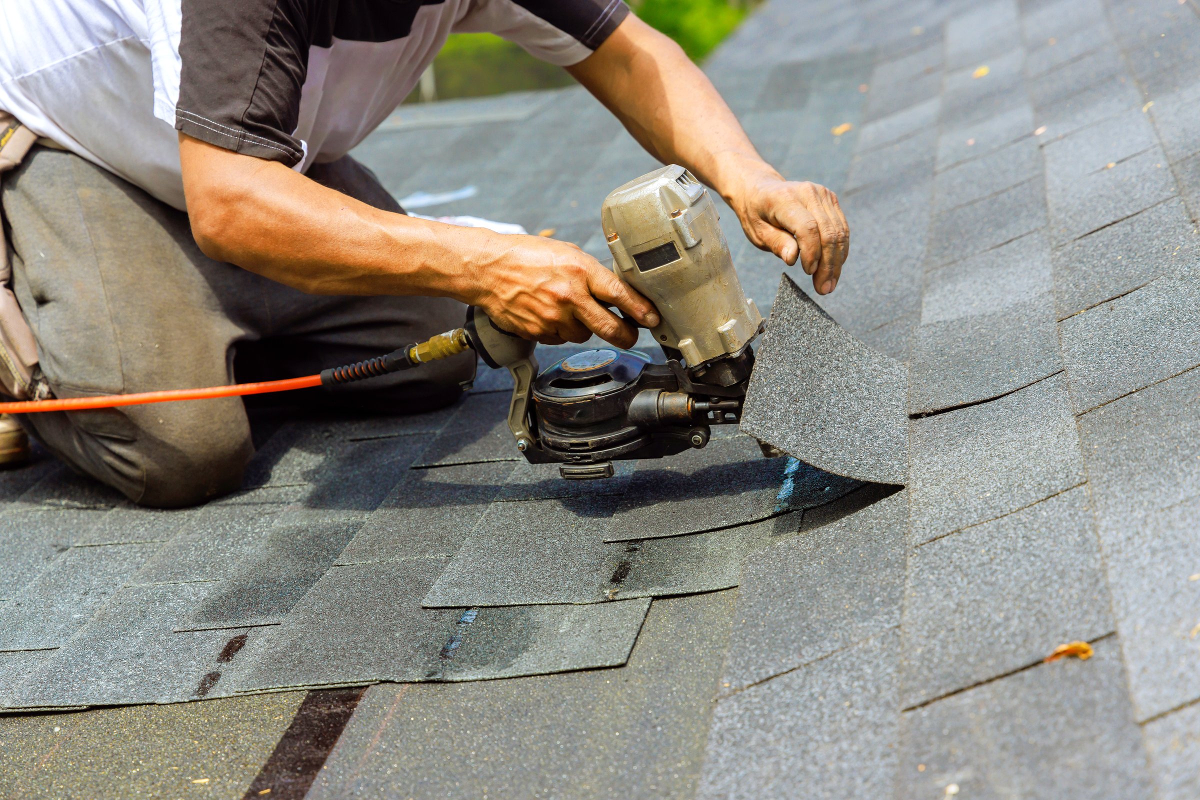 During installation of new bitumen shingles, construction roofer used pneumatic air nail gun