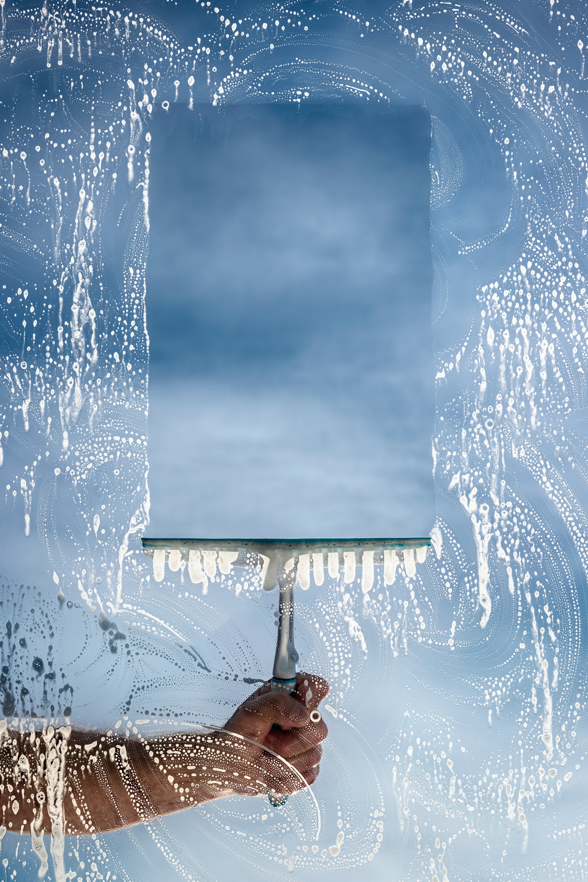 Window cleaner using a squeegee to wash a window with clear blue sky background