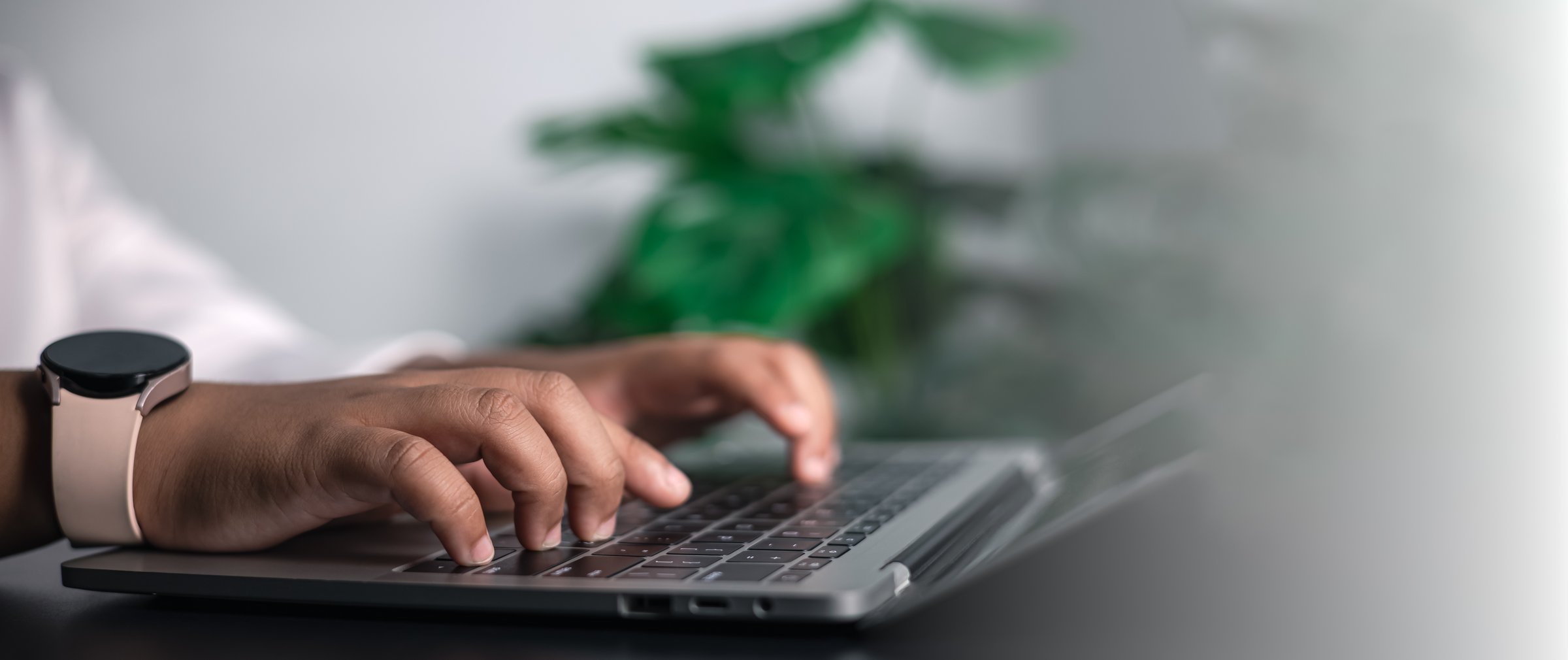 Close-up of hands wearing a smartwatch typing on a laptop keyboard, symbolizing remote work, online education, business communication, and modern productivity at home.