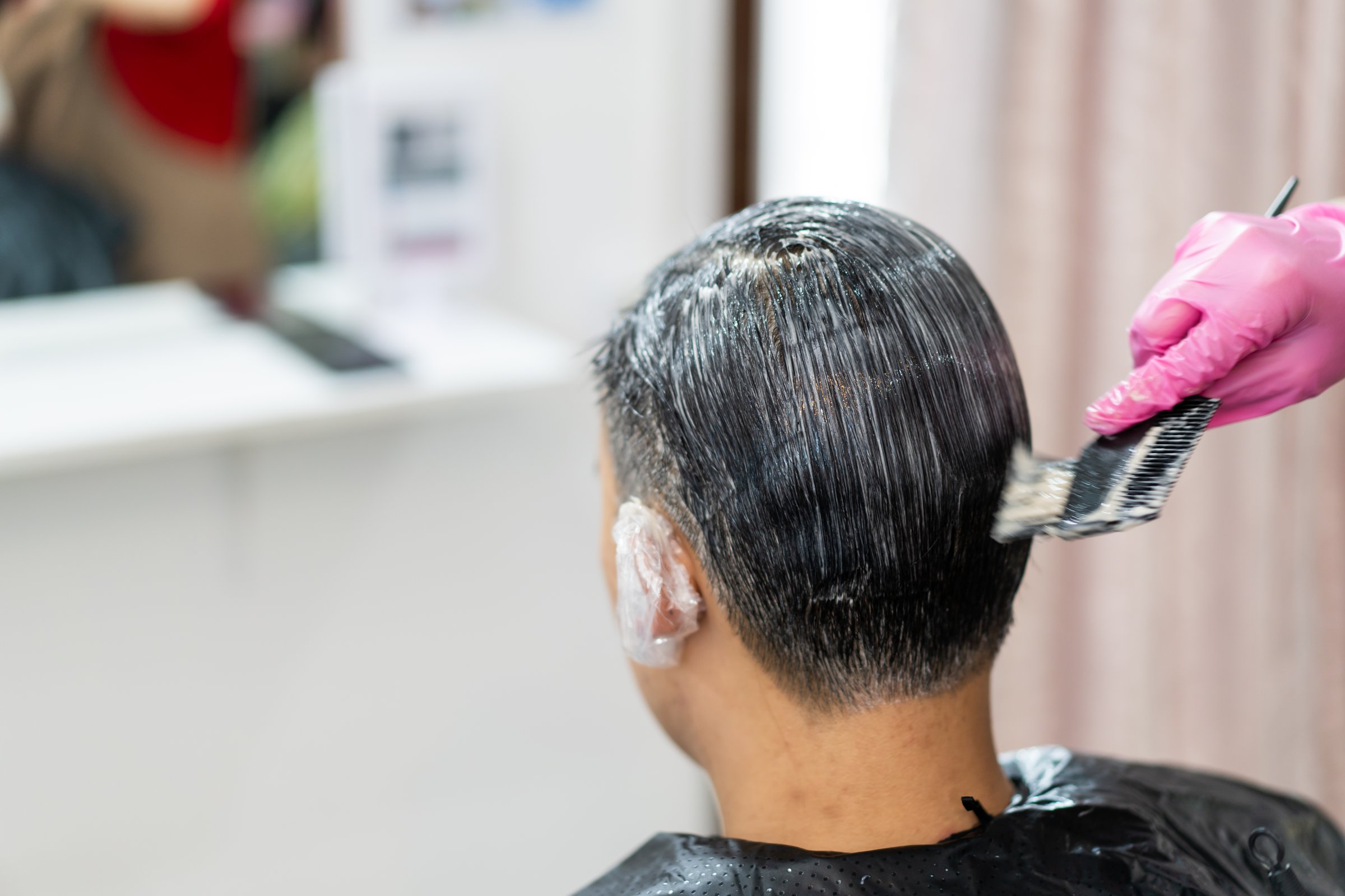 Asian young man making a hair dye at hair salon and spa. Professional hair stylist coloring - dying hair in male salon.