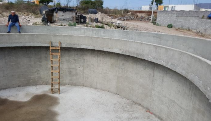 Large empty concrete tank with a wooden ladder inside, and a man sitting at the top edge.
