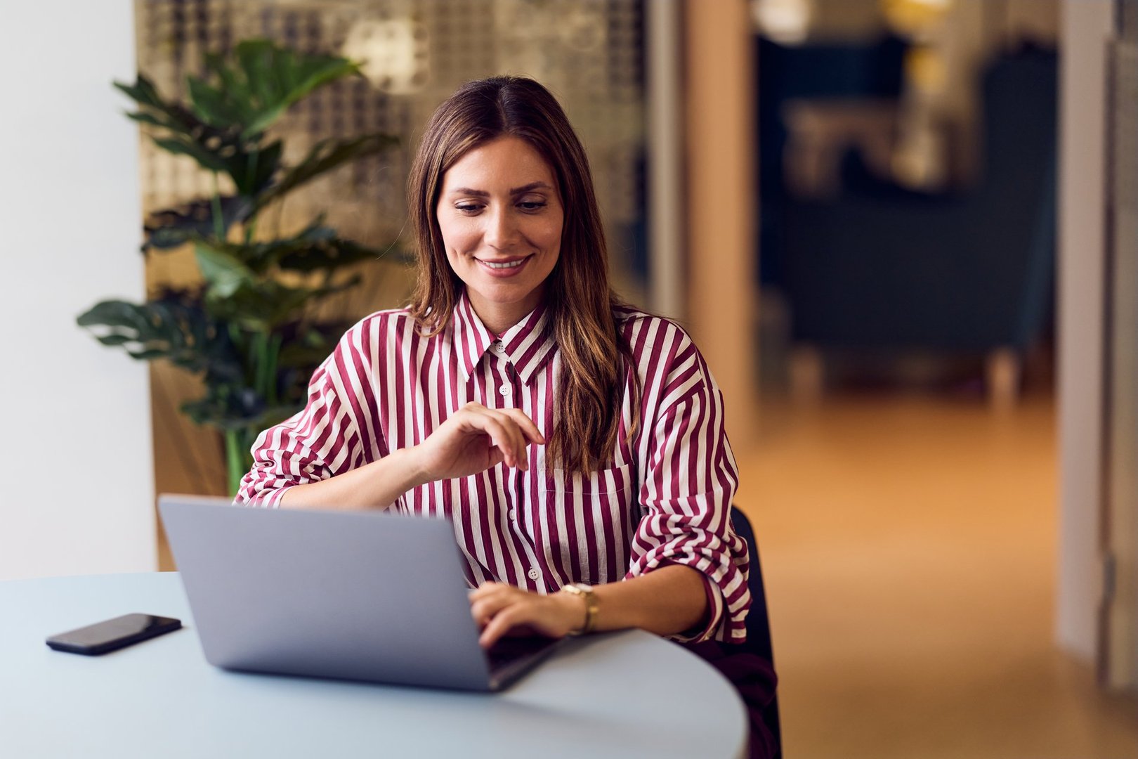 Focused professional woman using a laptop in a bright, stylish office environment.