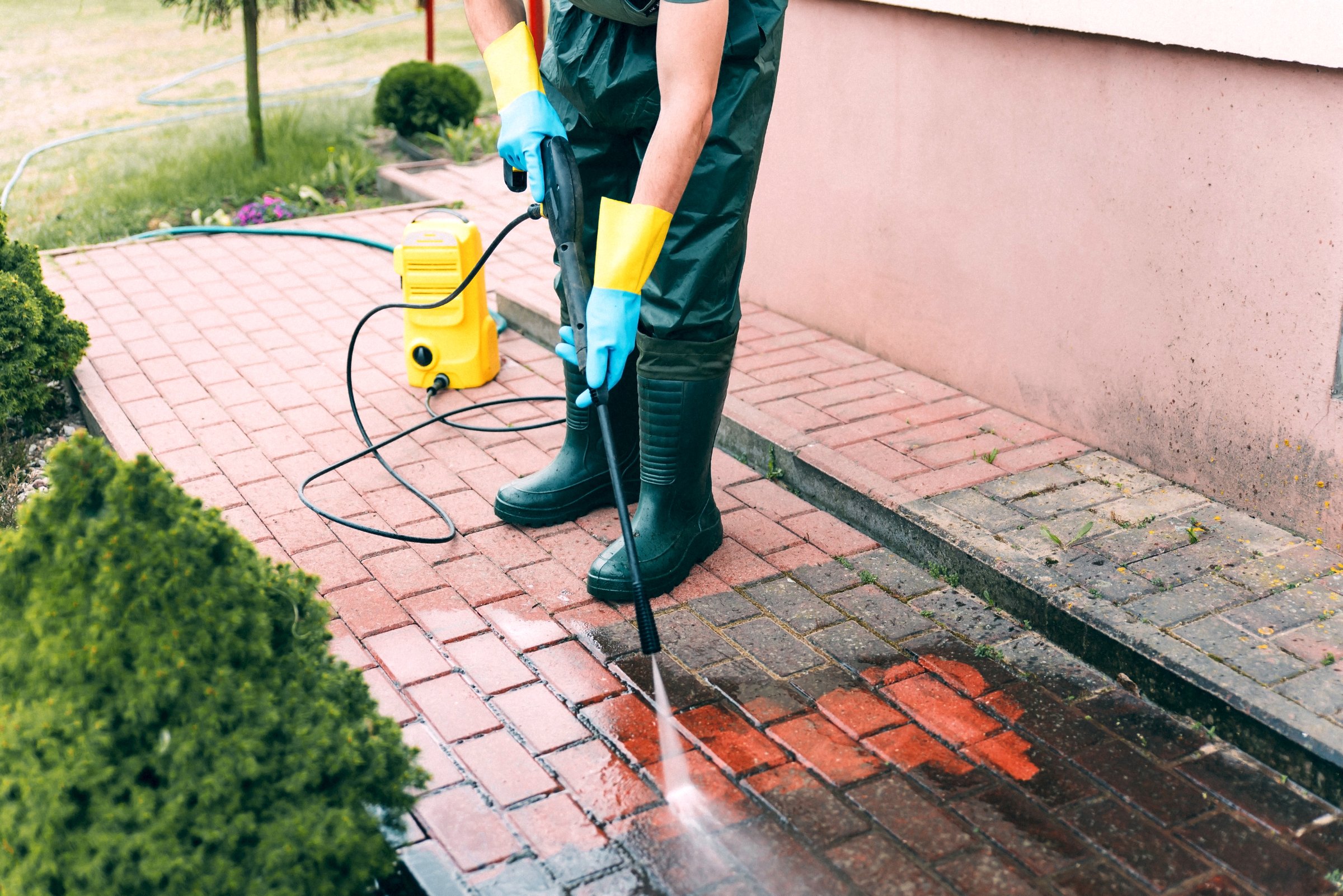 Man cleaning concrete pavement block using high pressure water cleaner