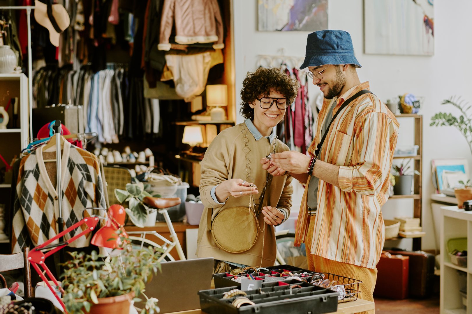 Friends exploring vintage store shelves, admiring various items and collectibles. Clothing racks and eclectic decor create cozy environment, fostering casual, friendly atmosphere