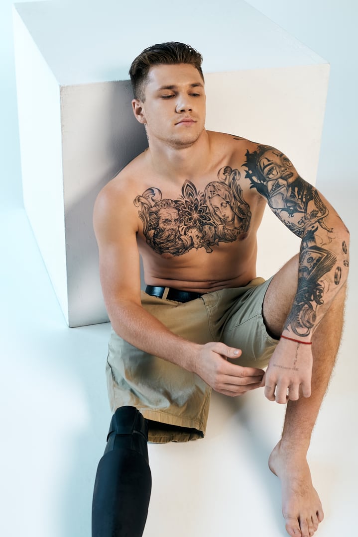 A young man sits confidently, highlighting his strength and style with a tattooed arm and an artificial limb.