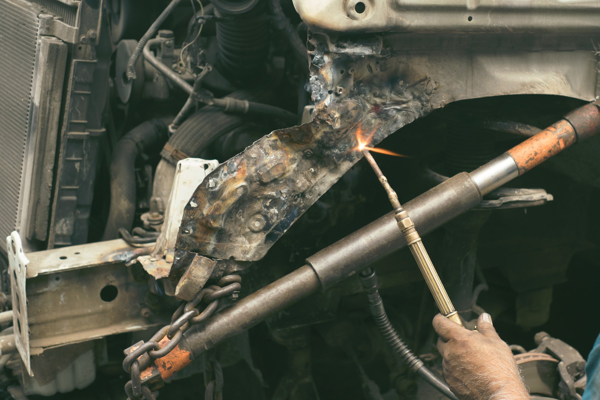 Mechanic welding a damaged car frame in an auto repair workshop.