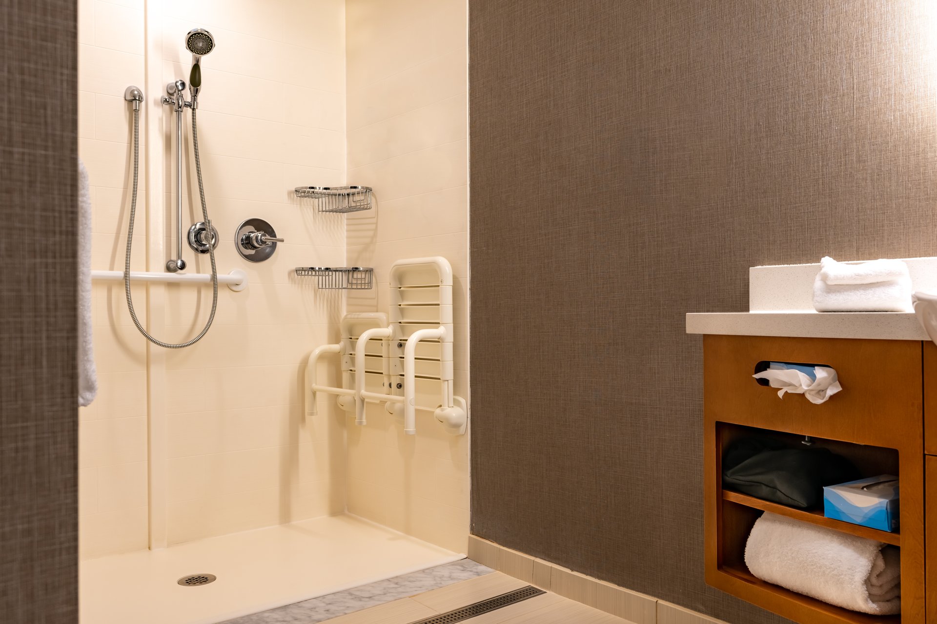Wheelchair accessible hotel bathroom shower with tile floor and walls.