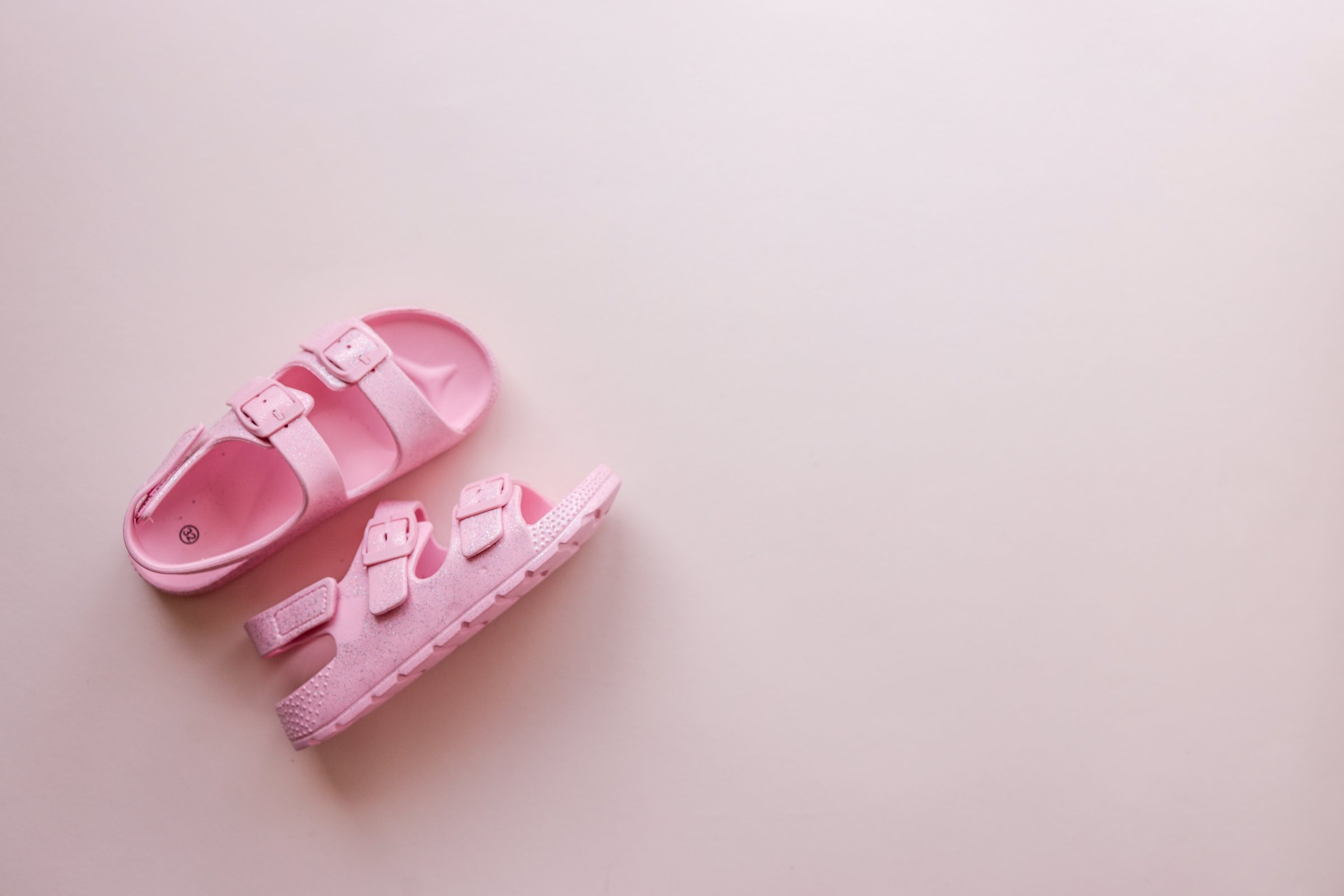 Pair of pink glittery children's sandals placed on a soft pastel background with empty space. Minimalist composition ideal for advertising or design mockups.