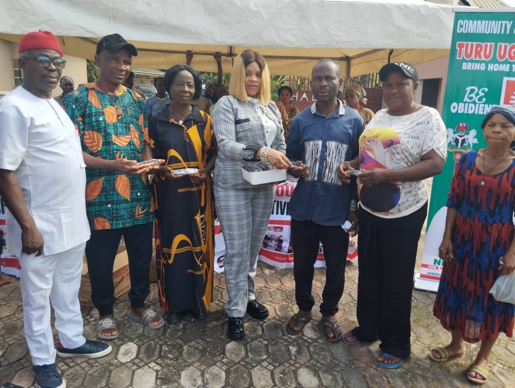 Group of people holding items in a community event under a tent, standing in front of a banner promoting a local initiative.