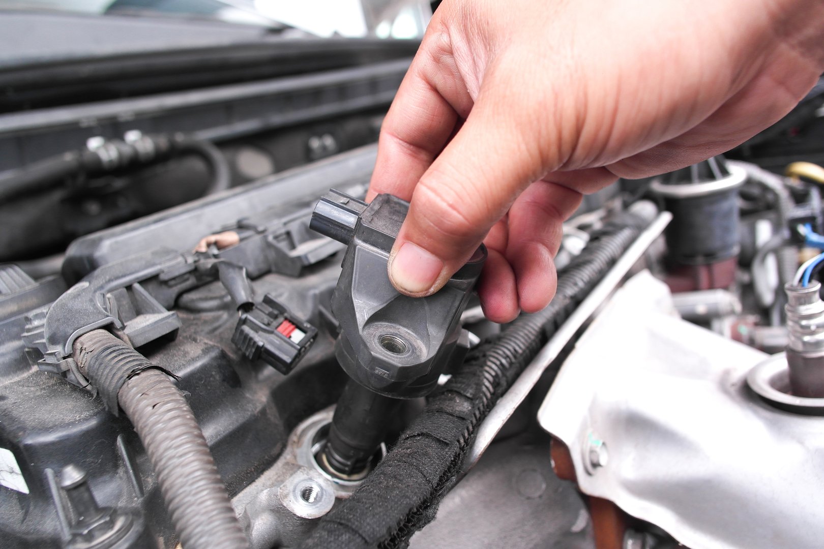 Mechanic hand replacing ignition coil on car engine, concept of engine repair, spark plug maintenance, automotive service, car diagnostics, and vehicle performance tuning