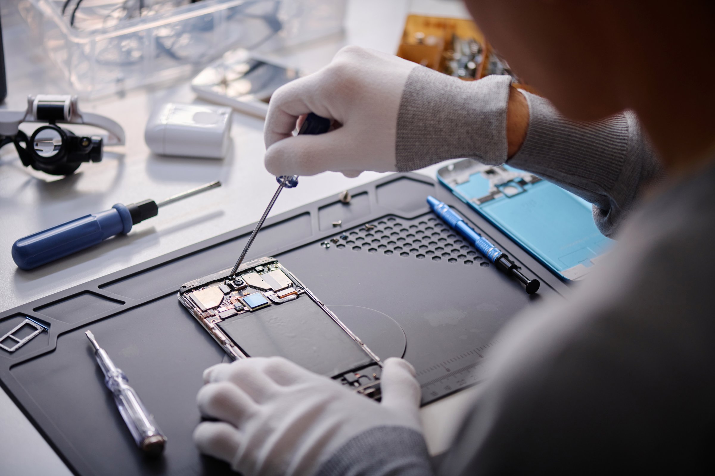 Over shoulder shot of unrecognizable technician repairing disassembled smartphone with screwdriver