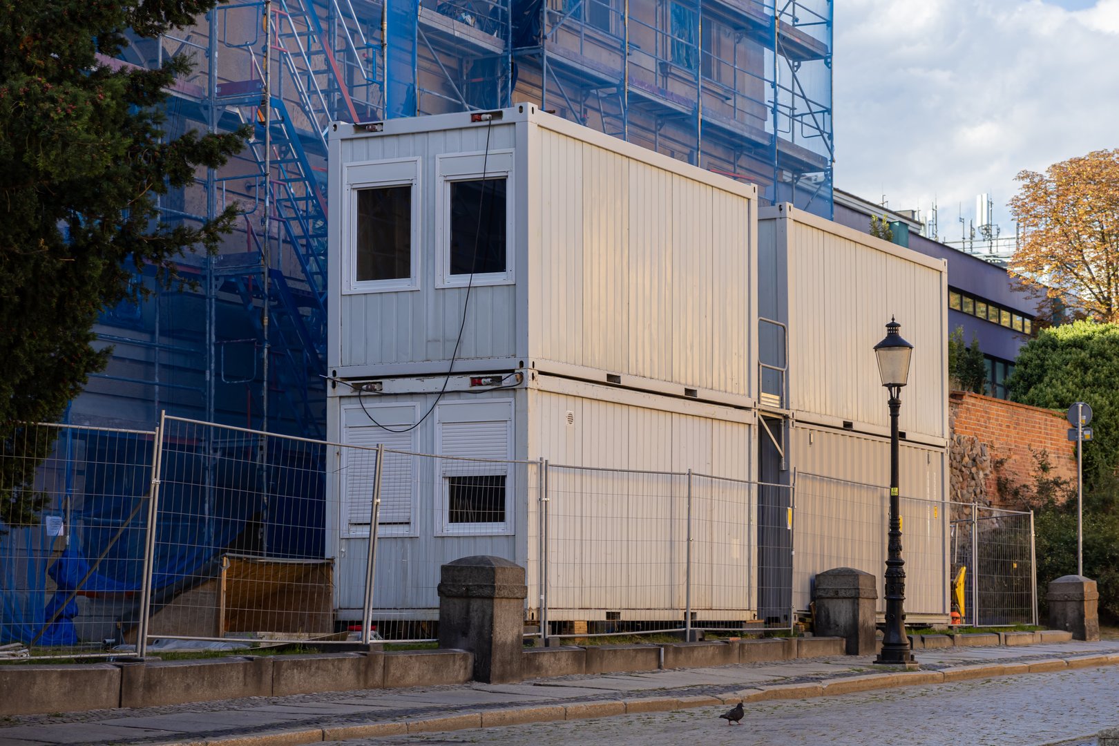 Stacked modular white container units with visible windows provide crucial temporary office space and worker accommodation on an urban construction site with scaffolding