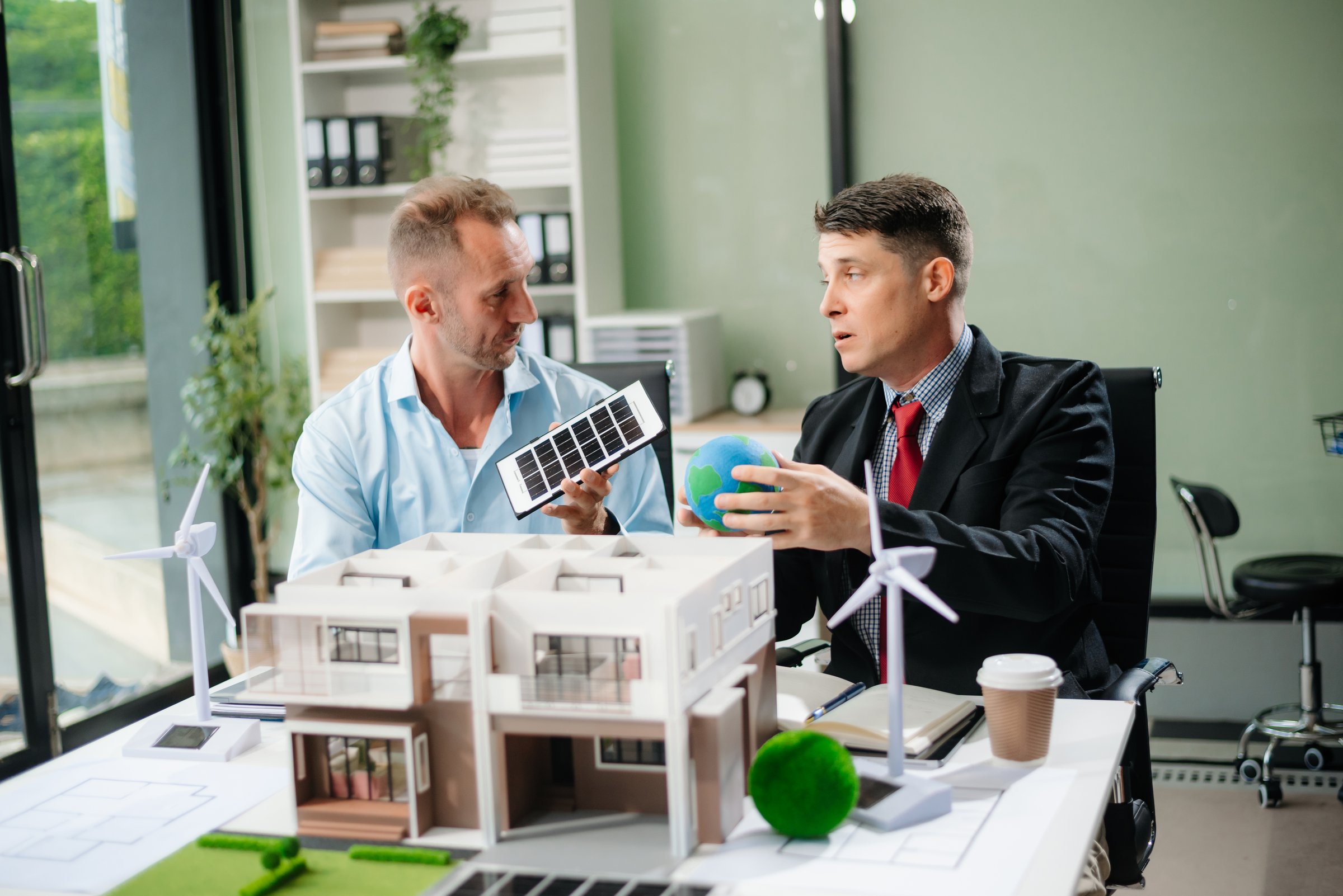 Experts collaborate on renewable energy solutions with house models, wind turbines, and solar panels, emphasizing green design and innovation.