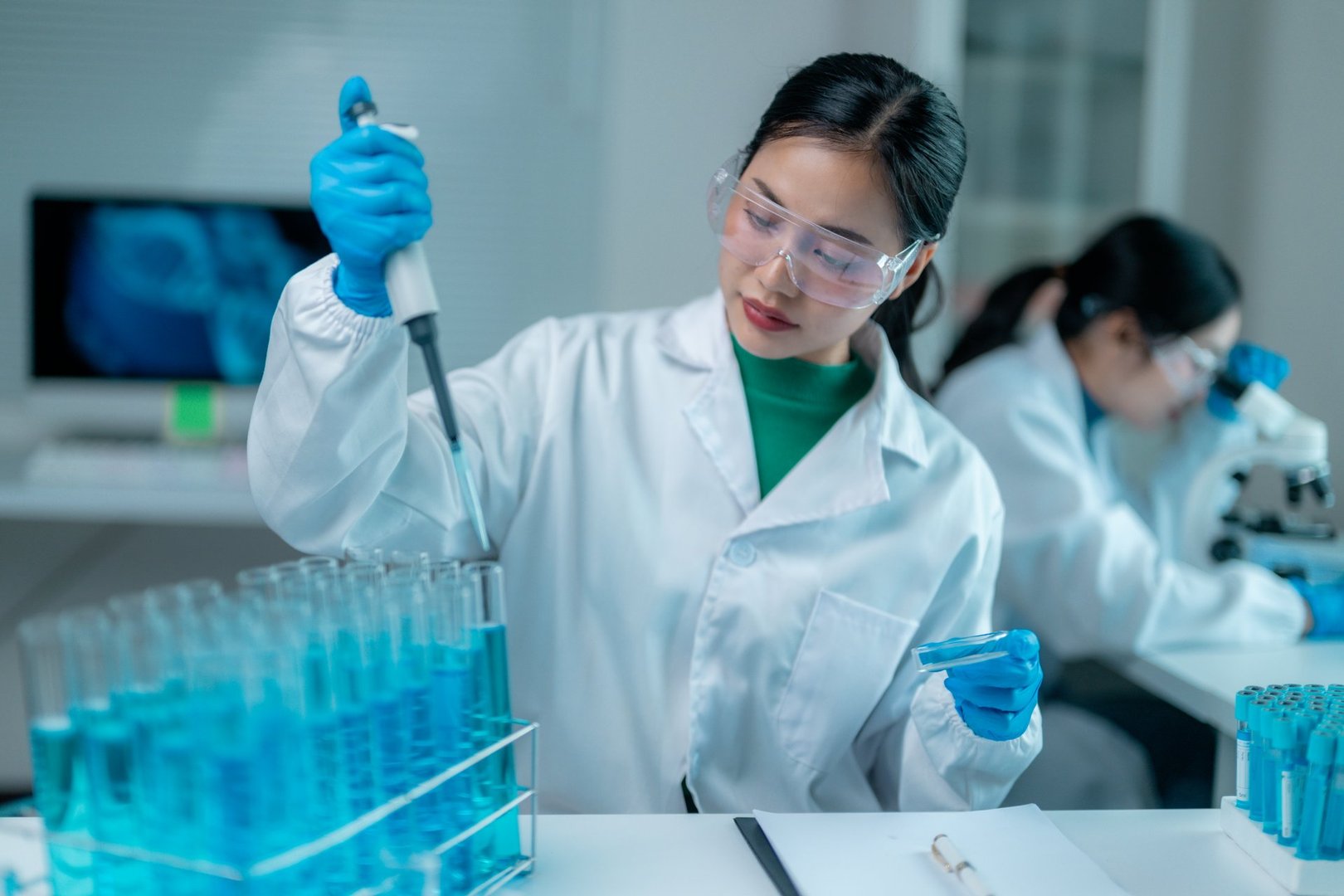 Two young adult scientists working in a laboratory, using pipettes and microscopes for research