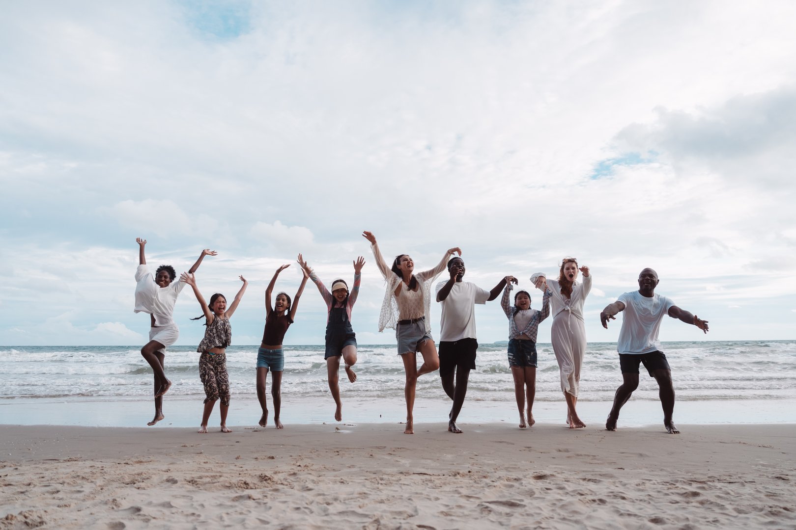 Happy diverse group of adults and children jumping together on the beach. Expressing family fun, freedom, vacation joy, and multicultural in nature.