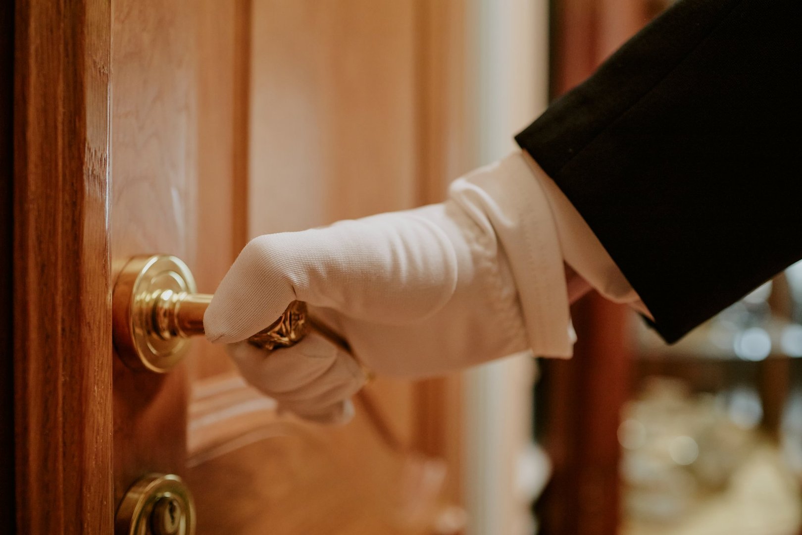 Caucasian middle aged man wearing glove turning brass doorknob with right hand, formal attire visible on arm, close up of hand and door, luxury service concept