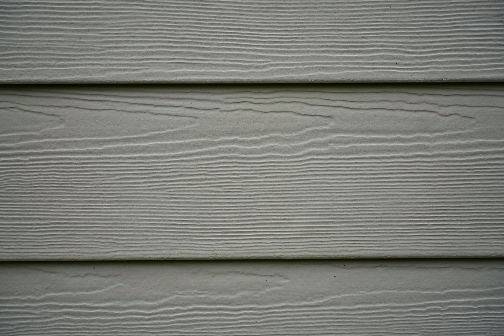 Detailed close-up image of beige horizontal vinyl siding with subtle wood grain texture. The pattern highlights the durability and aesthetic appeal of synthetic cladding commonly used in residential architecture.