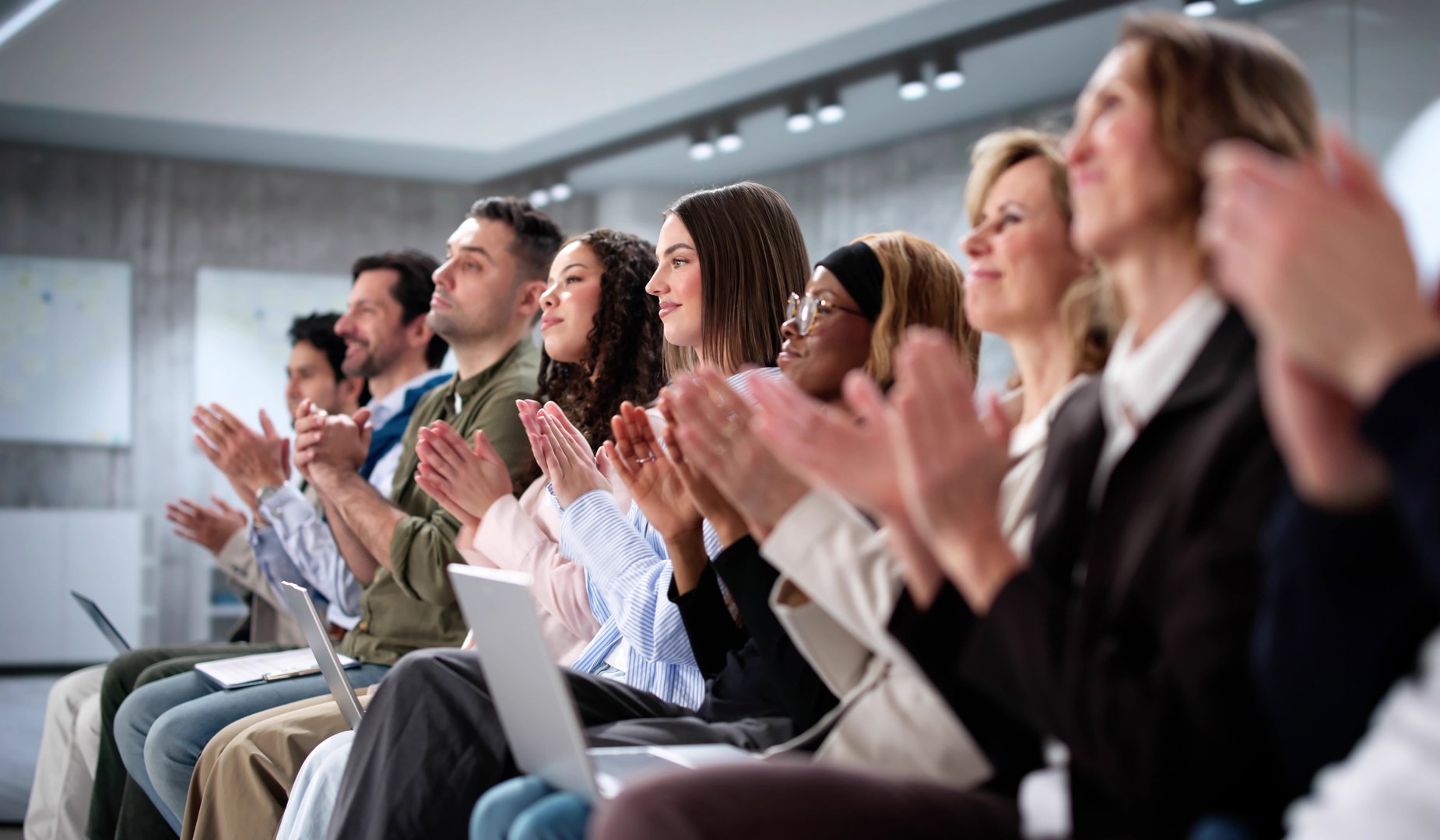 Smartly dressed audience of diverse business professionals applauding at seminar.