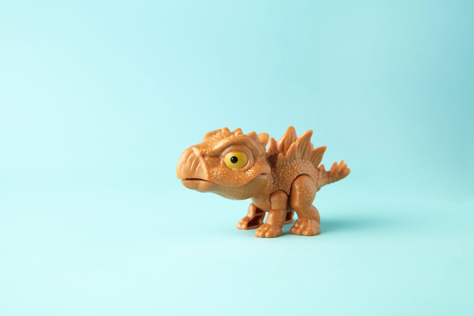 Small and cute plastic stegosaurus toy on cyan background