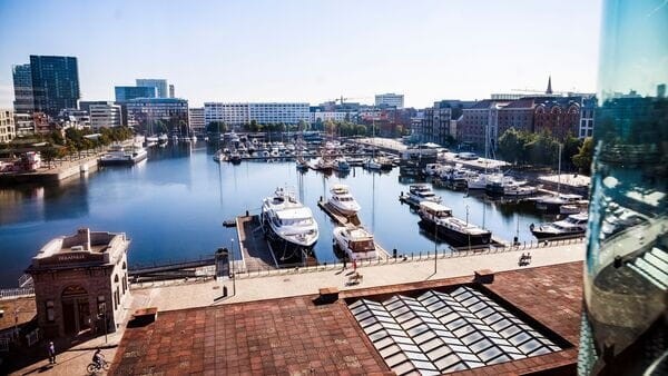 Boats and yachts docked in a tranquil marina surrounded by modern buildings on a sunny day.